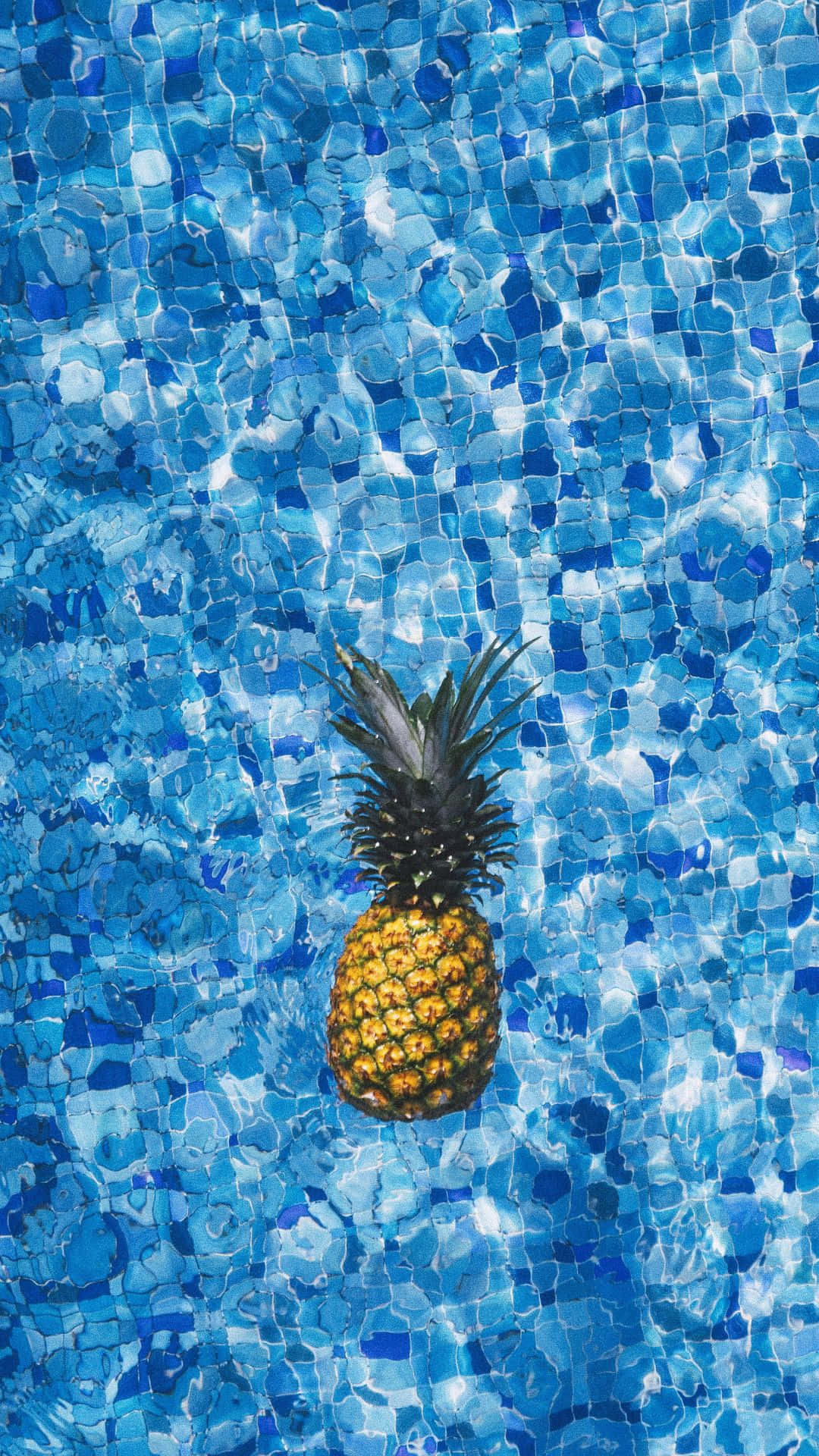 Android Summer 桌布 壁紙 — 一個成熟的鳳梨在陽光普照的藍色馬賽克瓷磚泳池中靜靜漂浮。
