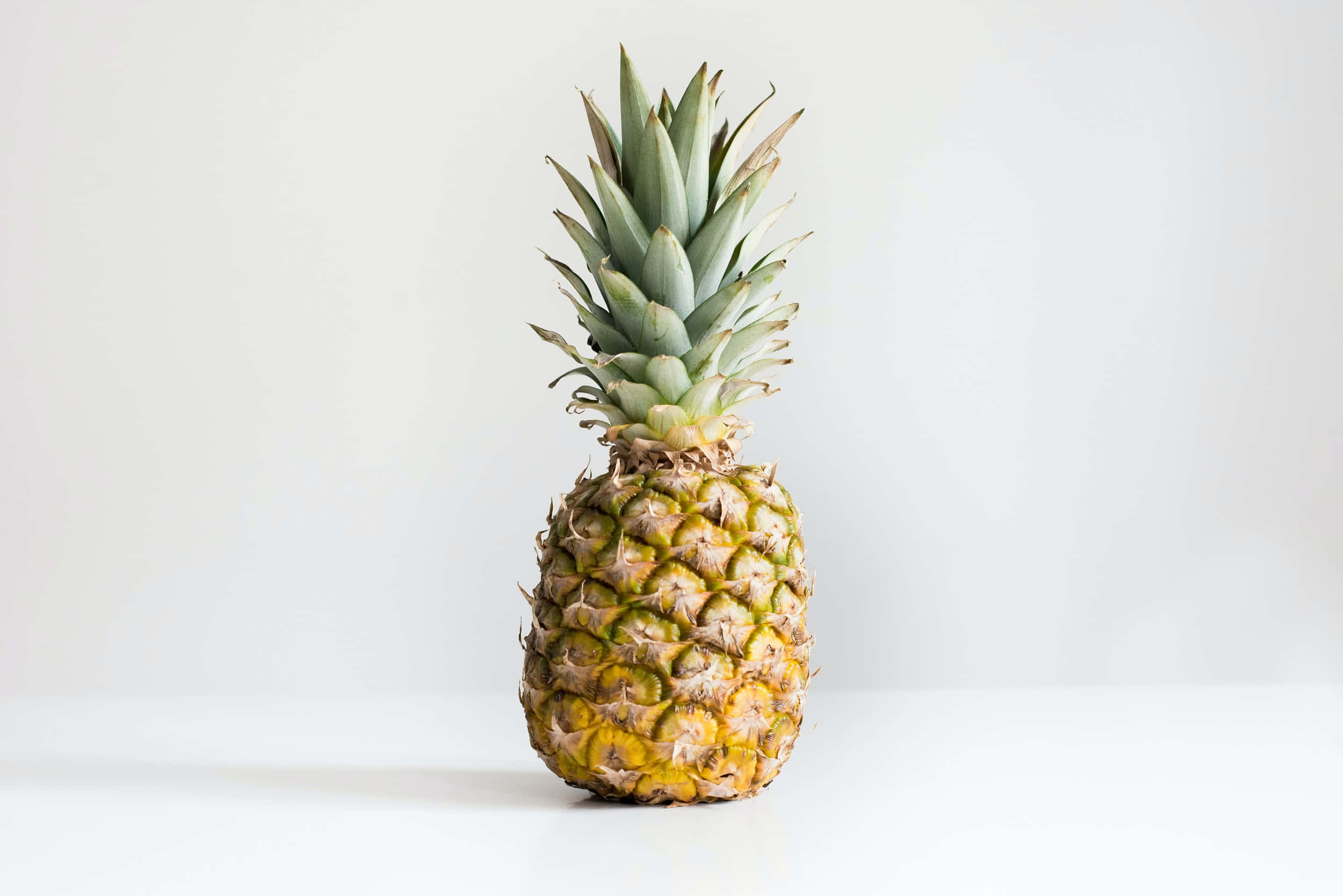Pineapple 桌布 壁紙 — 一個成熟的鳳梨帶有綠色冠部，居中放置在白色表面上，背景為純白色。