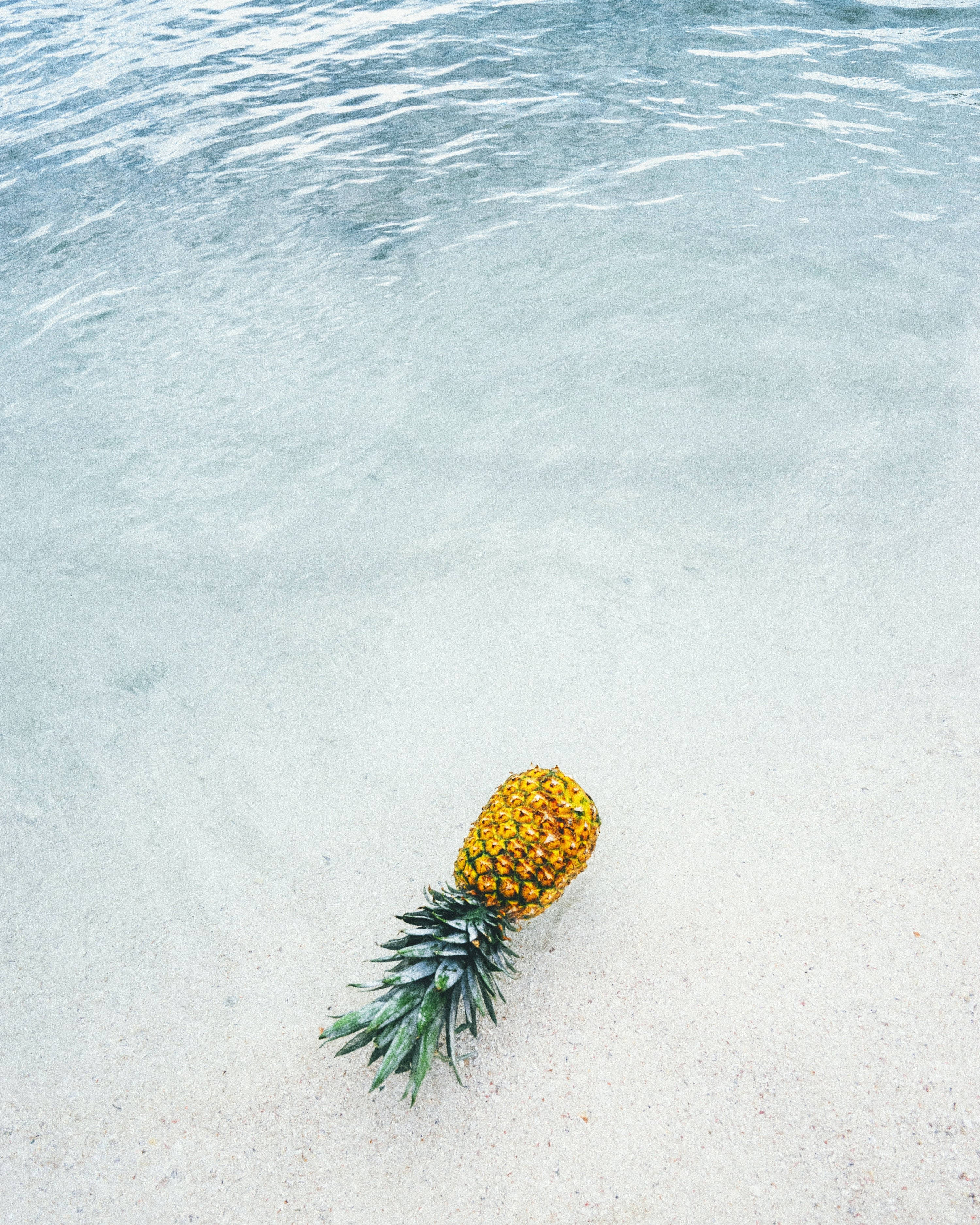 Best Summer 桌布 壁紙 — 一個成熟的鳳梨放在白色沙灘上，旁邊是清澈的藍綠色海水。