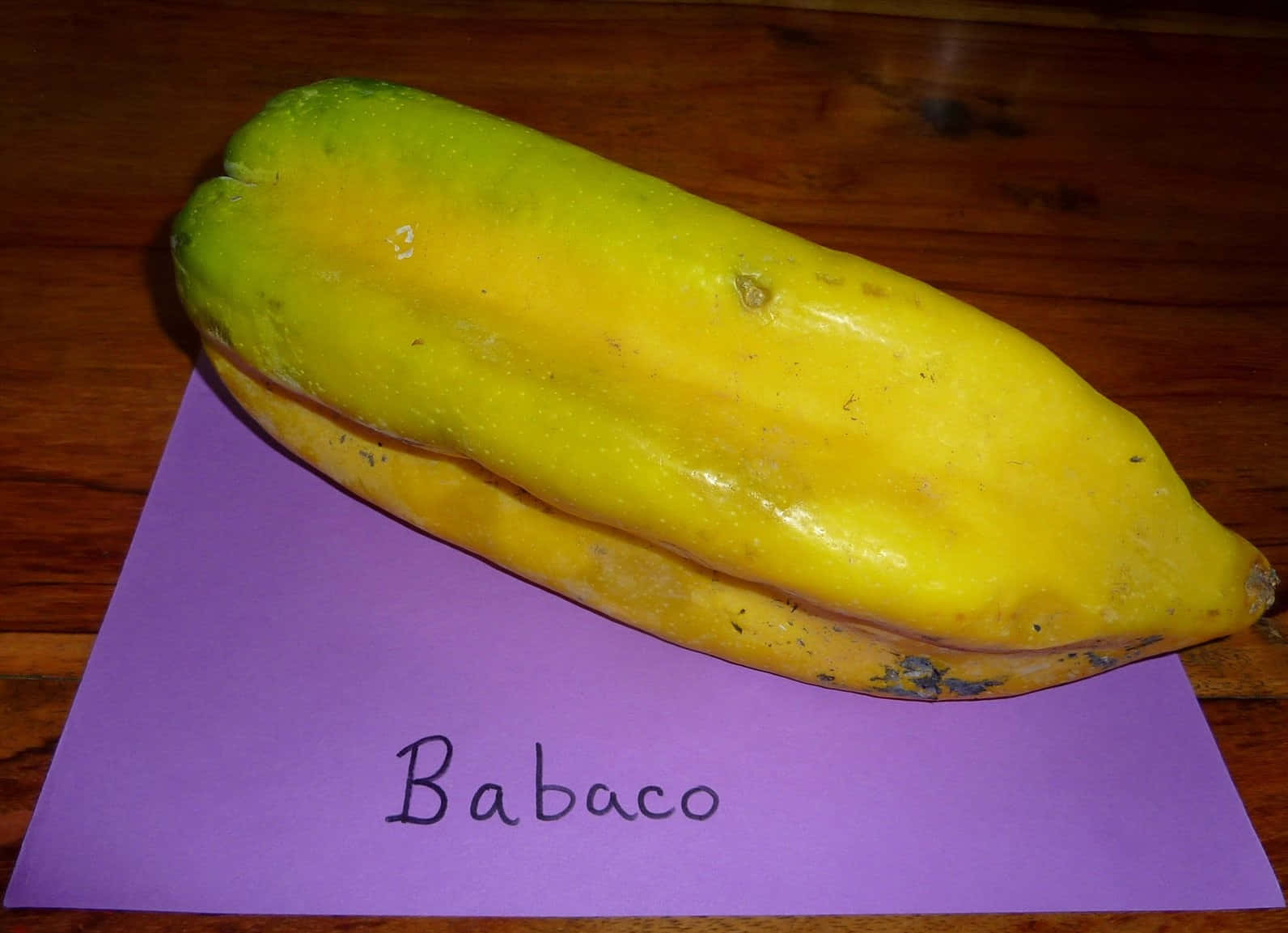 Fruit 桌布 壁紙 — 一個成熟的黃綠色babaco果實放在一個標有babaco的紫色紙上，置於木質表面。