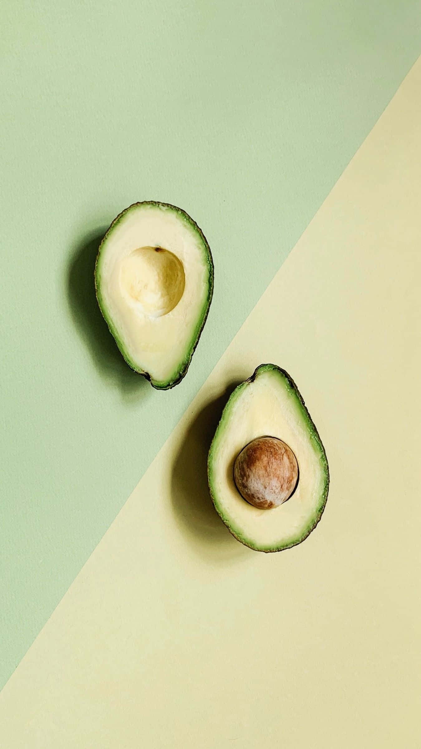 Avocado iPhone 桌布 壁紙 — 一個成熟酪梨的兩半（連核）放在一個分為綠色和奶油色的背景上。