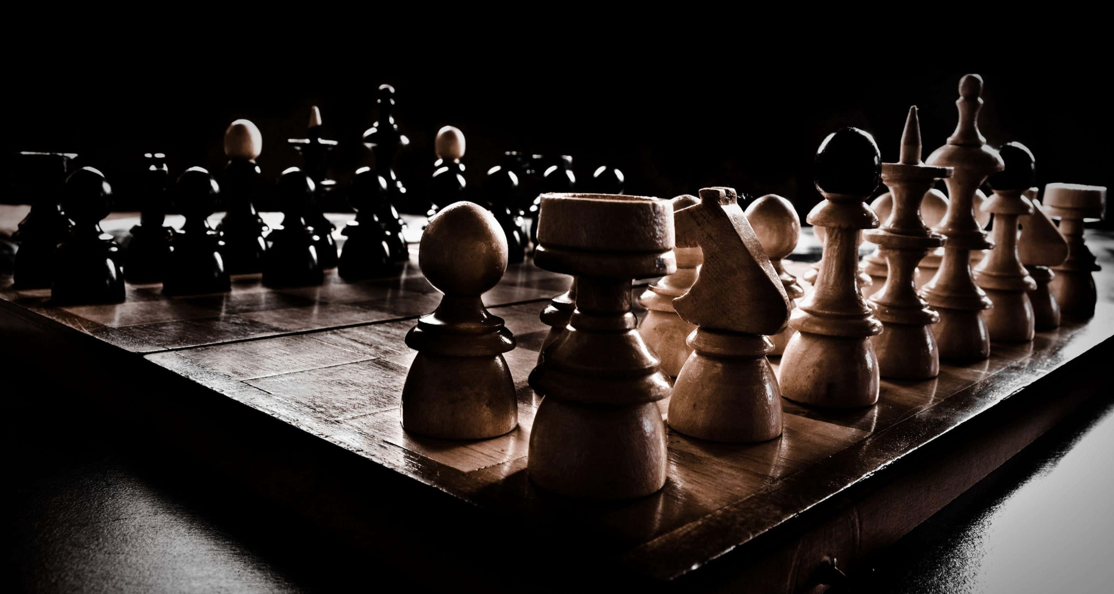 西洋棋 桌布 壁紙 — 一個戲劇性的低角度拍攝，木製西洋棋棋子放在棋盤上，在強烈的聚光燈下，背景為黑色。
