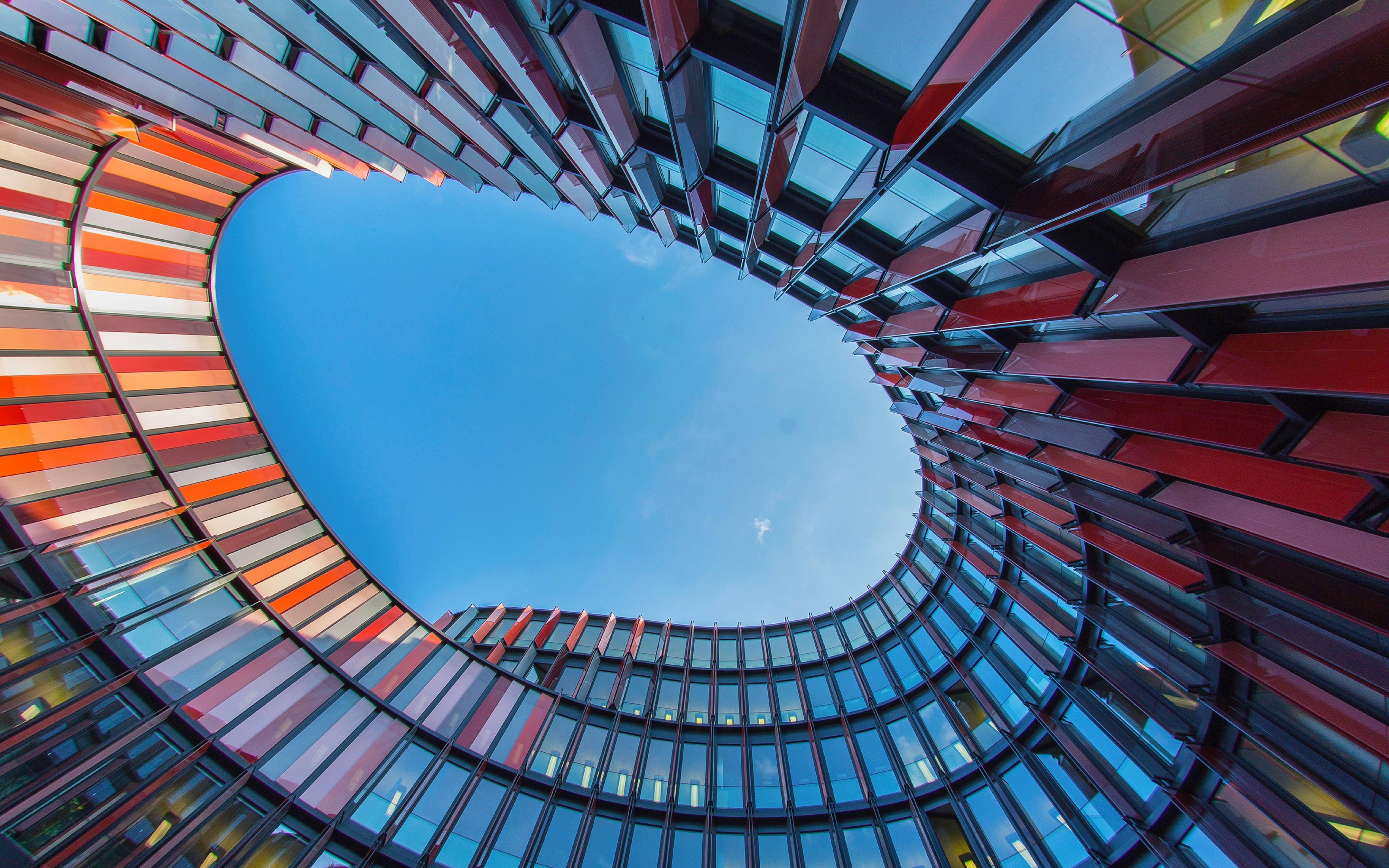 Architecture 桌布 壁紙 — 一個戲劇性的低角度視圖，現代圓形建築帶有彩色玻璃面板，框住清澈的藍天。