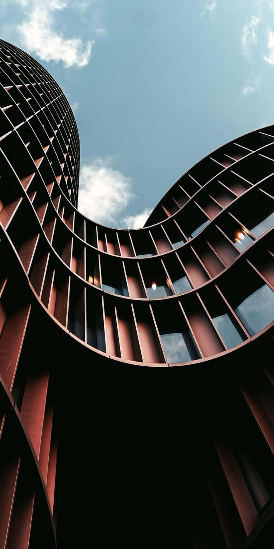 Building 桌布 壁紙 — 一個戲劇性的低角度視角，展示了一座現代曲線建築，帶有紅褐色金屬面板，背景是明亮的藍天和散落的雲朵。