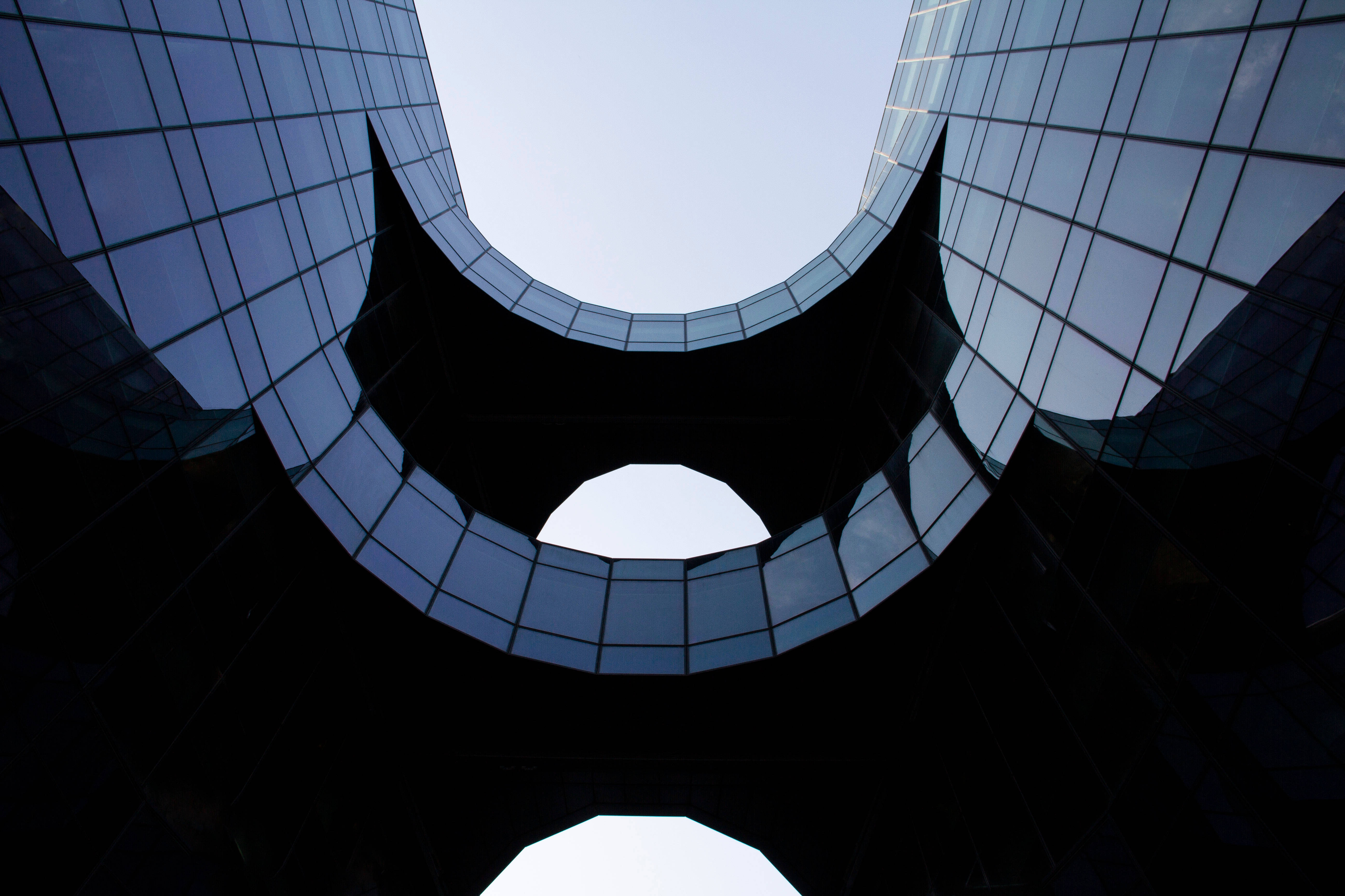 more 桌布 壁紙 — 一個戲劇性的低角度視角，現代玻璃建築的弧形外牆框住了明亮的天空。