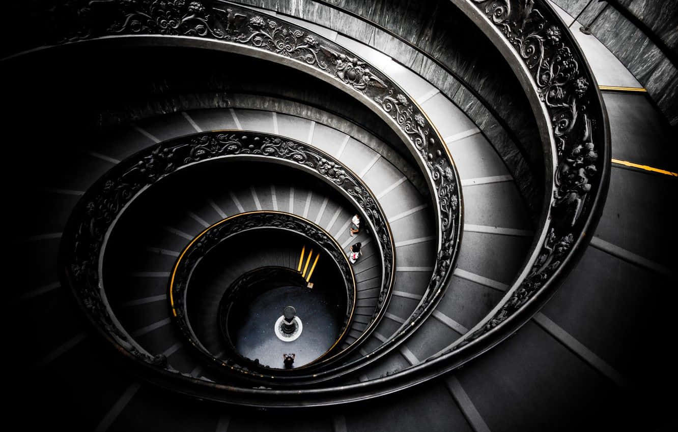 stairs 桌布 壁紙 — 一個戲劇性的俯視圖，展示了一個宏偉的螺旋樓梯，帶有華麗的欄杆和微小的人物正在攀登其蜿蜒的台階。