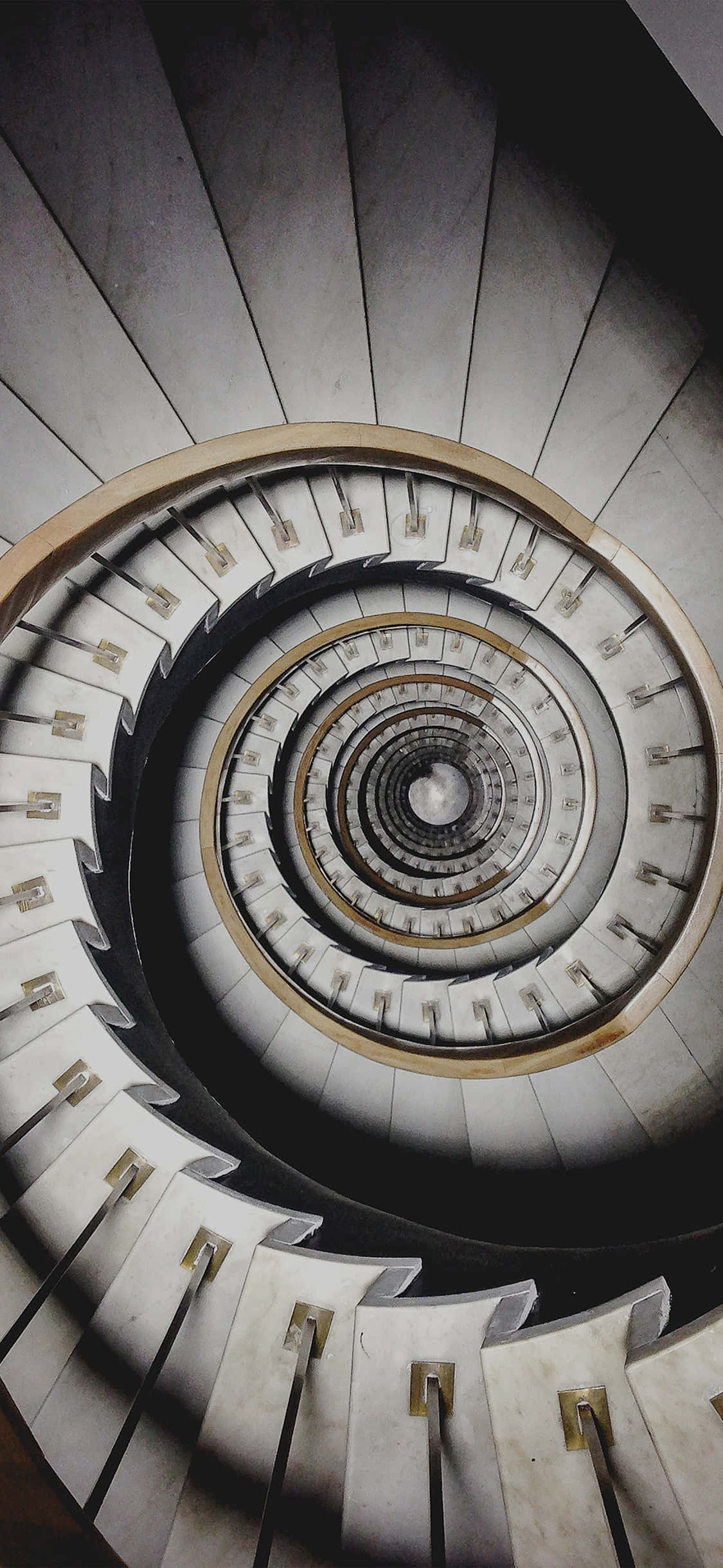 Spiral 桌布 壁紙 — 一個戲劇性的俯視圖，顯示螺旋形混凝土樓梯向下延伸至陰暗的黑暗中。