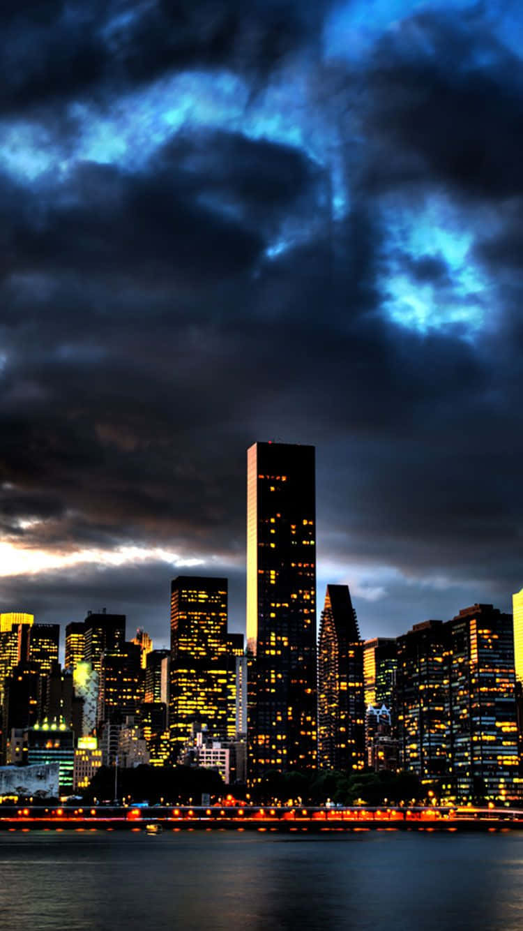 City iPhone 桌布 壁紙 — 一個戲劇性的城市天際線夜景，高聳的摩天大樓在暴風雨般的藍黑天空下被金色窗戶照亮。