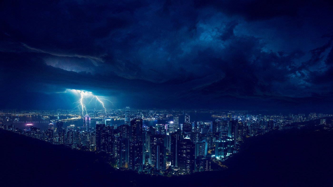 閃電 桌布 壁紙 — 一個戲劇性的夜晚城市景觀，被一道強大的閃電照亮，劈開黑暗的暴風雲，照耀在發光的摩天大樓之上。