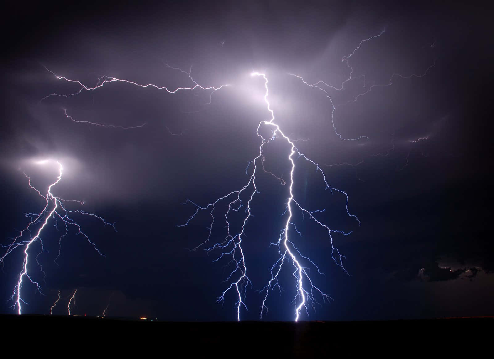 閃電 桌布 壁紙 — 一個戲劇性的夜空，被多道生動的閃電劈開，照亮了烏雲和遙遠的地平線。