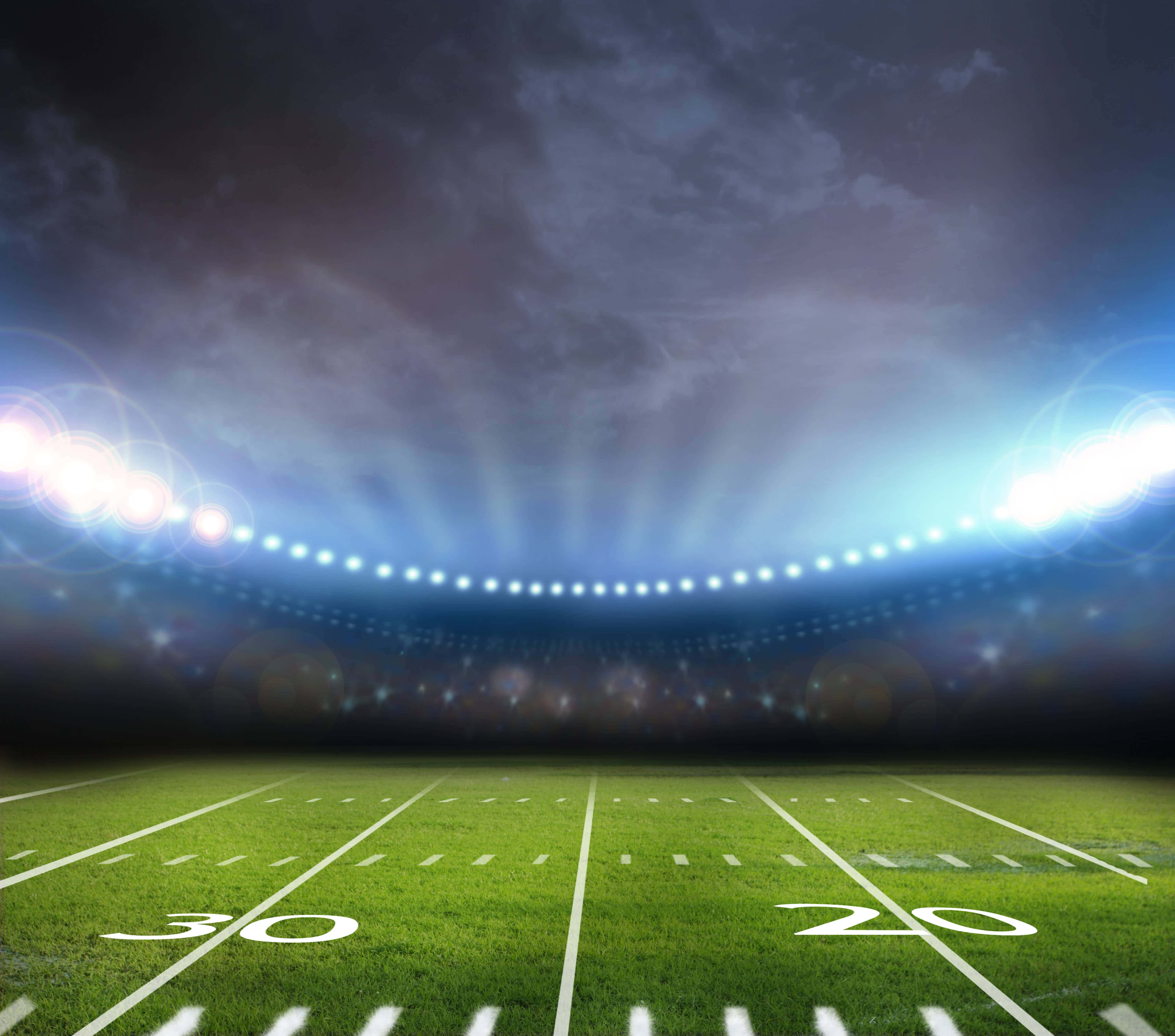 Football Field 桌布 壁紙 — 一個戲劇性的夜間足球場，明亮的泛光燈照亮了多雲天空下充滿活力的綠色場地。