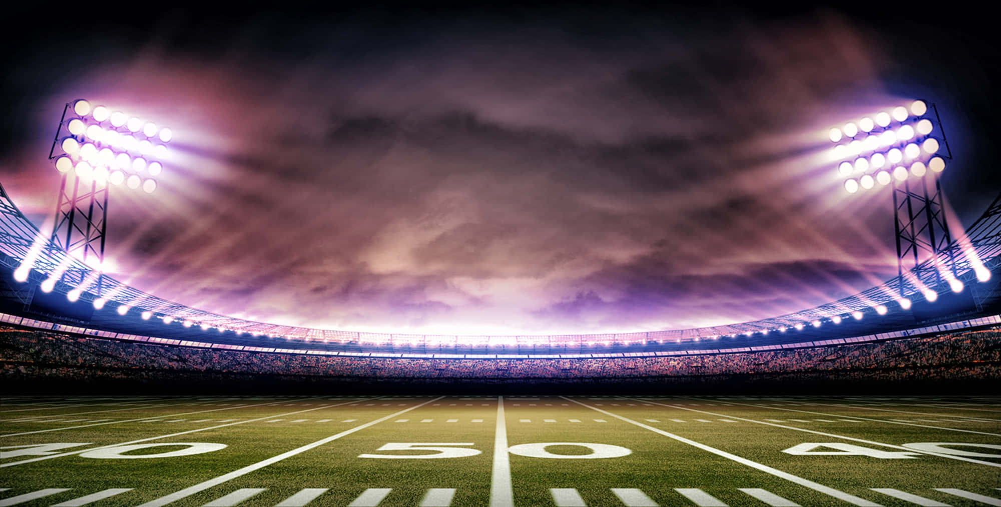 Football Field 桌布 壁紙 — 一個戲劇性的夜間足球場，由強力泛光燈照亮，光束穿過紫色雲層。