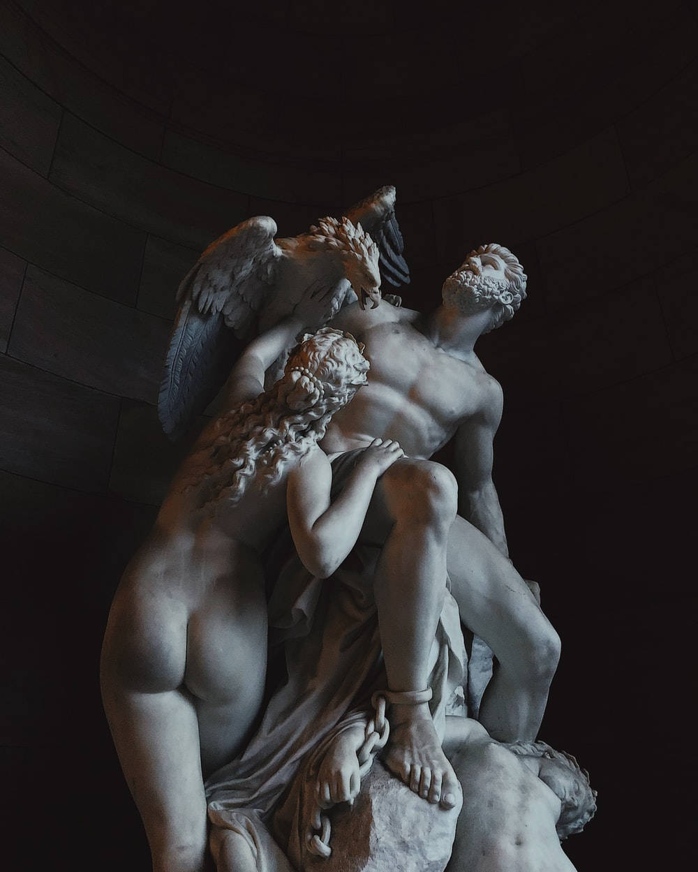 Sculpture 桌布 壁紙 — 一個戲劇性的大理石雕塑描繪了一個有翼的人物擁抱一個鬍鬚男，而一個被鎖鏈束縛的人物躺在下面一個光線昏暗的石室中。