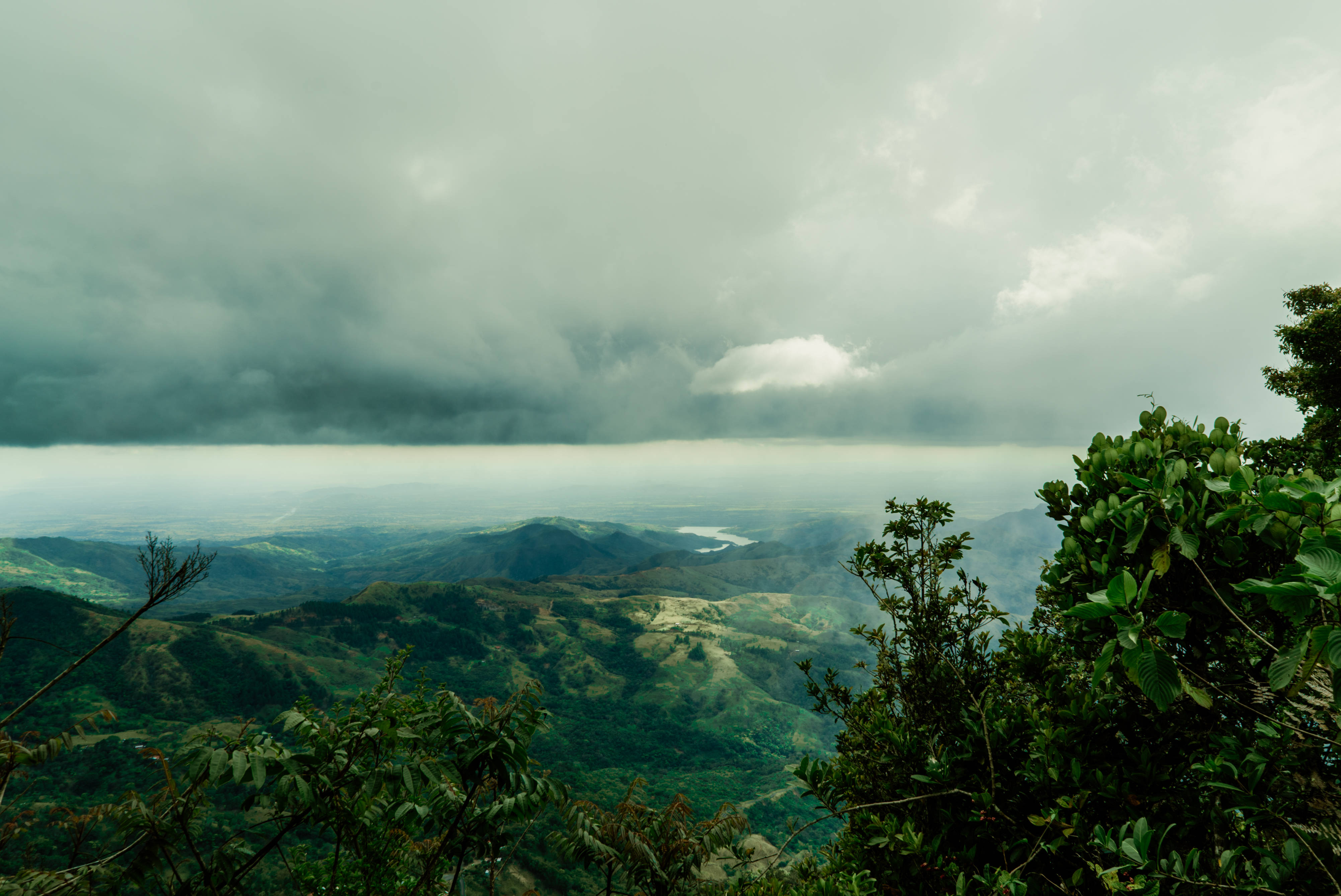 Panama 桌布 壁紙 — 一個戲劇性的山谷，籠罩在厚重的灰色雲層中，前景有茂密的綠色樹葉。