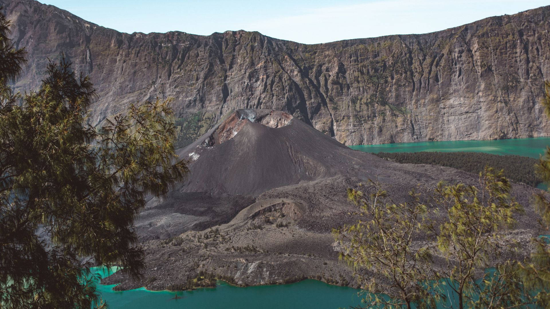 電腦 桌布 壁紙 — 一個戲劇性的火山口，充滿充滿活力的綠松石色海水，周圍是崎嶇的黑色懸崖，並以綠色樹葉為框架。