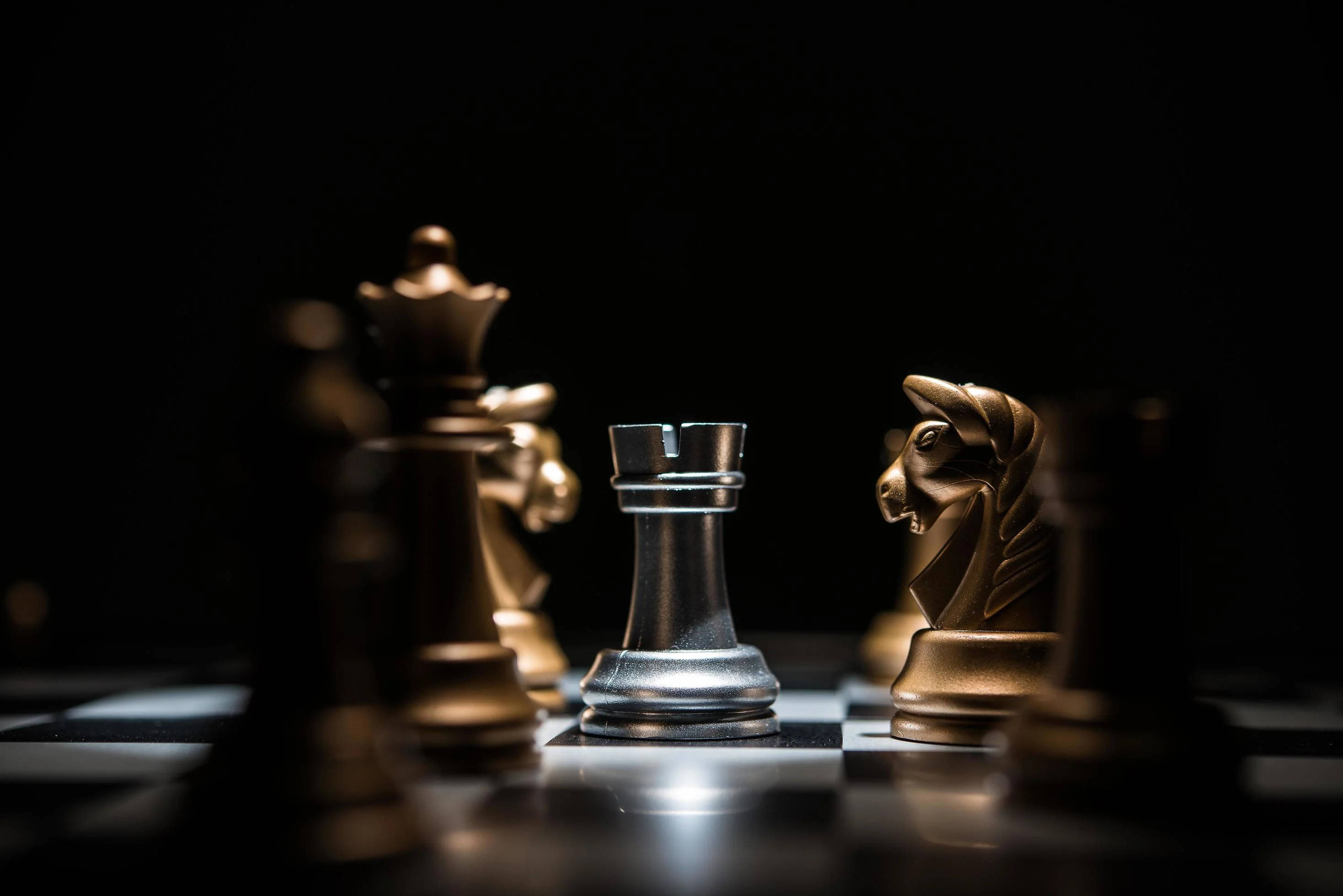 西洋棋 桌布 壁紙 — 一個戲劇性的特寫，棋盤上的銀色城堡和金色騎士在聚焦燈光下對峙。