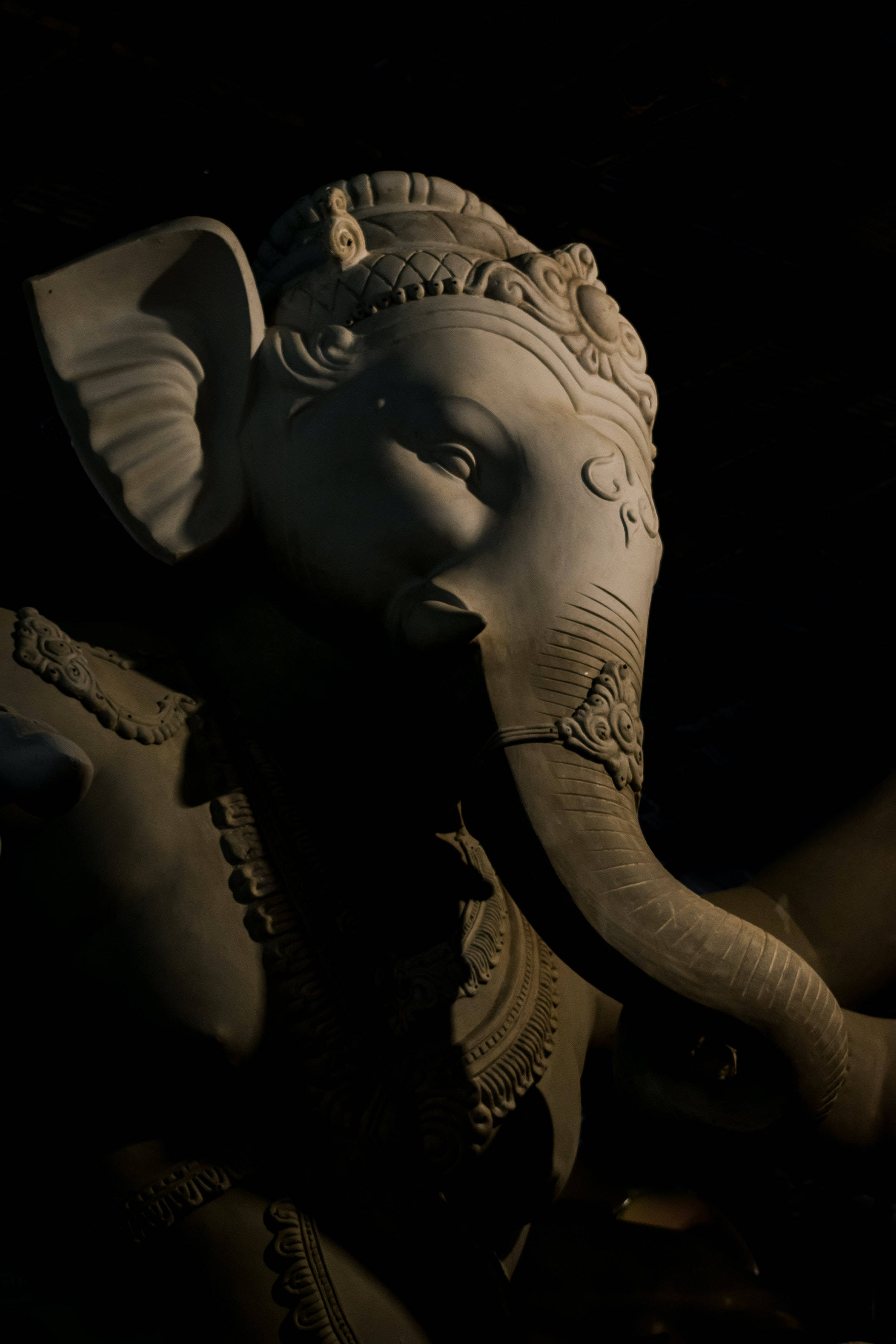 hindu iPhone 桌布 壁紙 — 一個戲劇性的特寫，石頭象神雕像在黑色背景下被聚焦光線照亮。