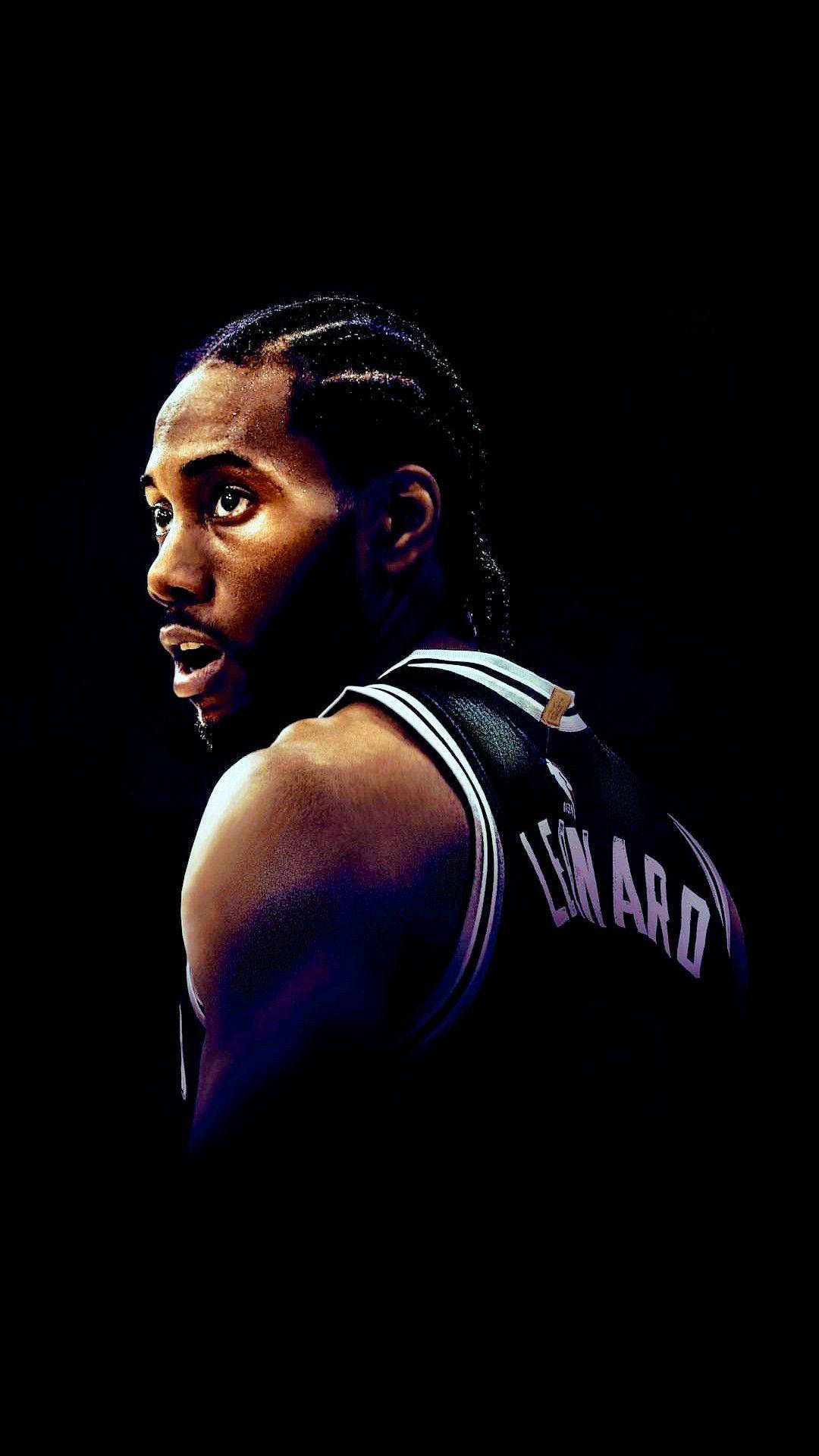 Kawhi 桌布 壁紙 — 一個戲劇性的特寫，籃球運動員Kawhi Leonard身穿黑色球衣，在黑暗背景中帶有強烈燈光。