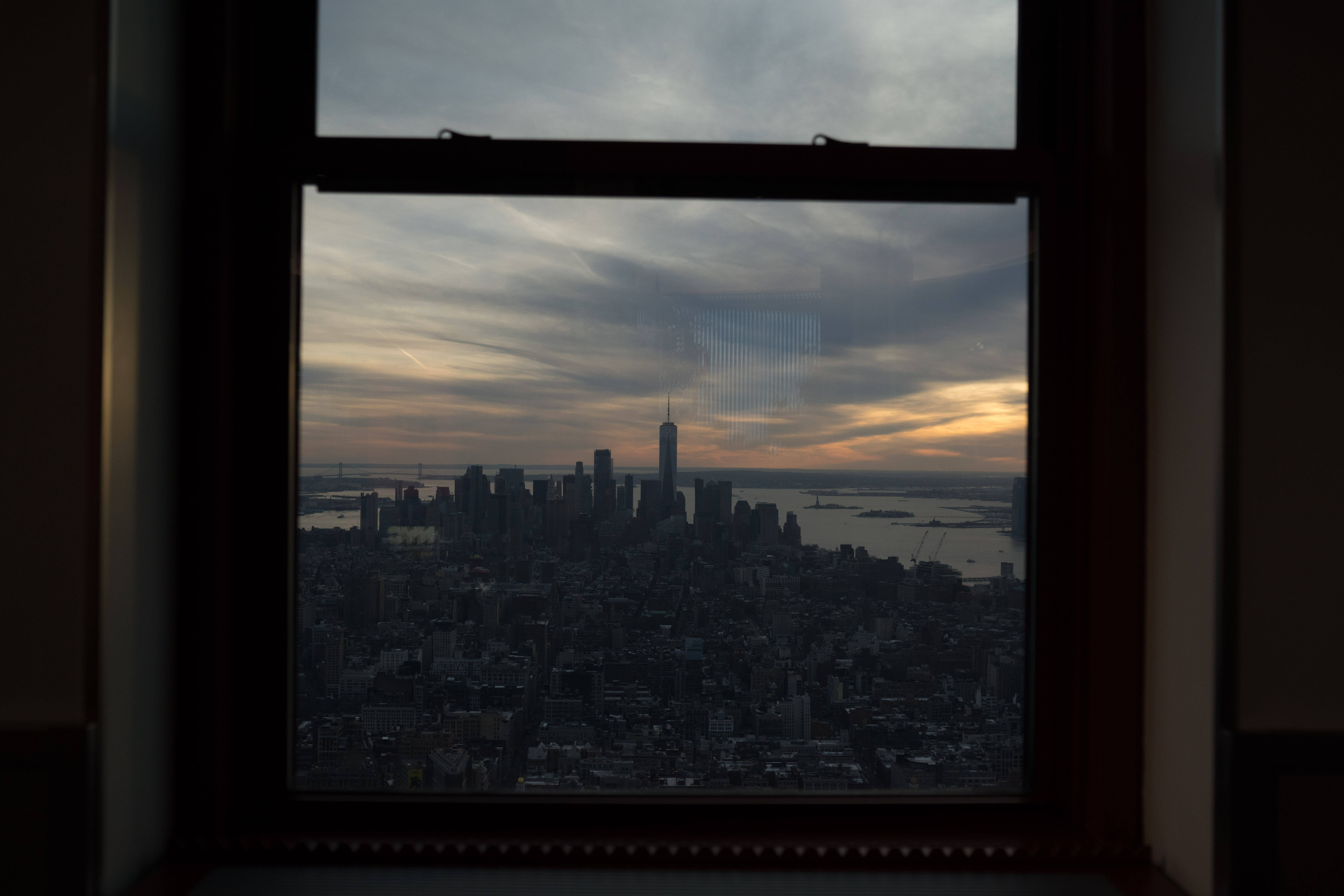 empire state 桌布 壁紙 — 一個戲劇性的紐約市天際線日落景觀，由深色木窗框住，雲彩橫掃天空。