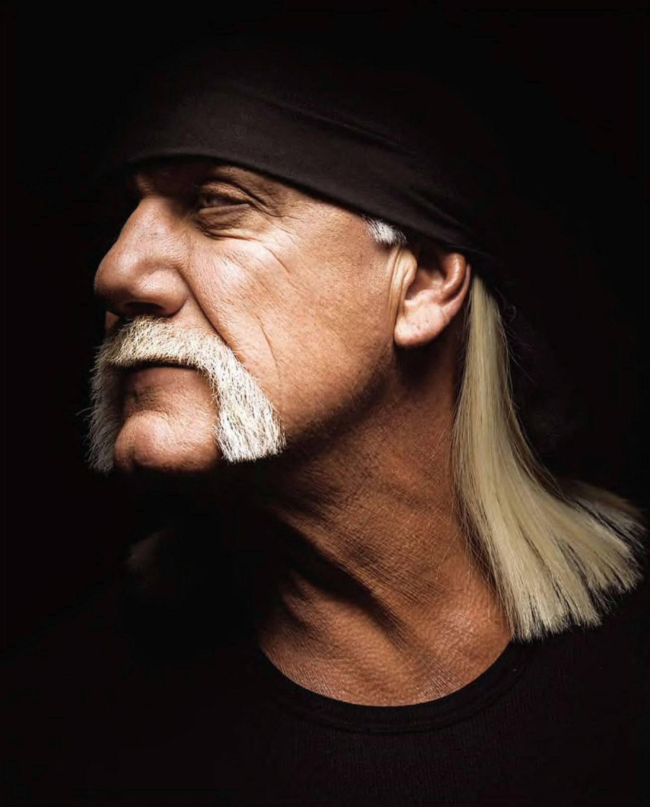Hulk Hogan 桌布 壁紙 — 一個戲劇性的肖像，一個留著白色山羊鬍和長金髮的男人，戴著黑色頭帶，背景是深色。