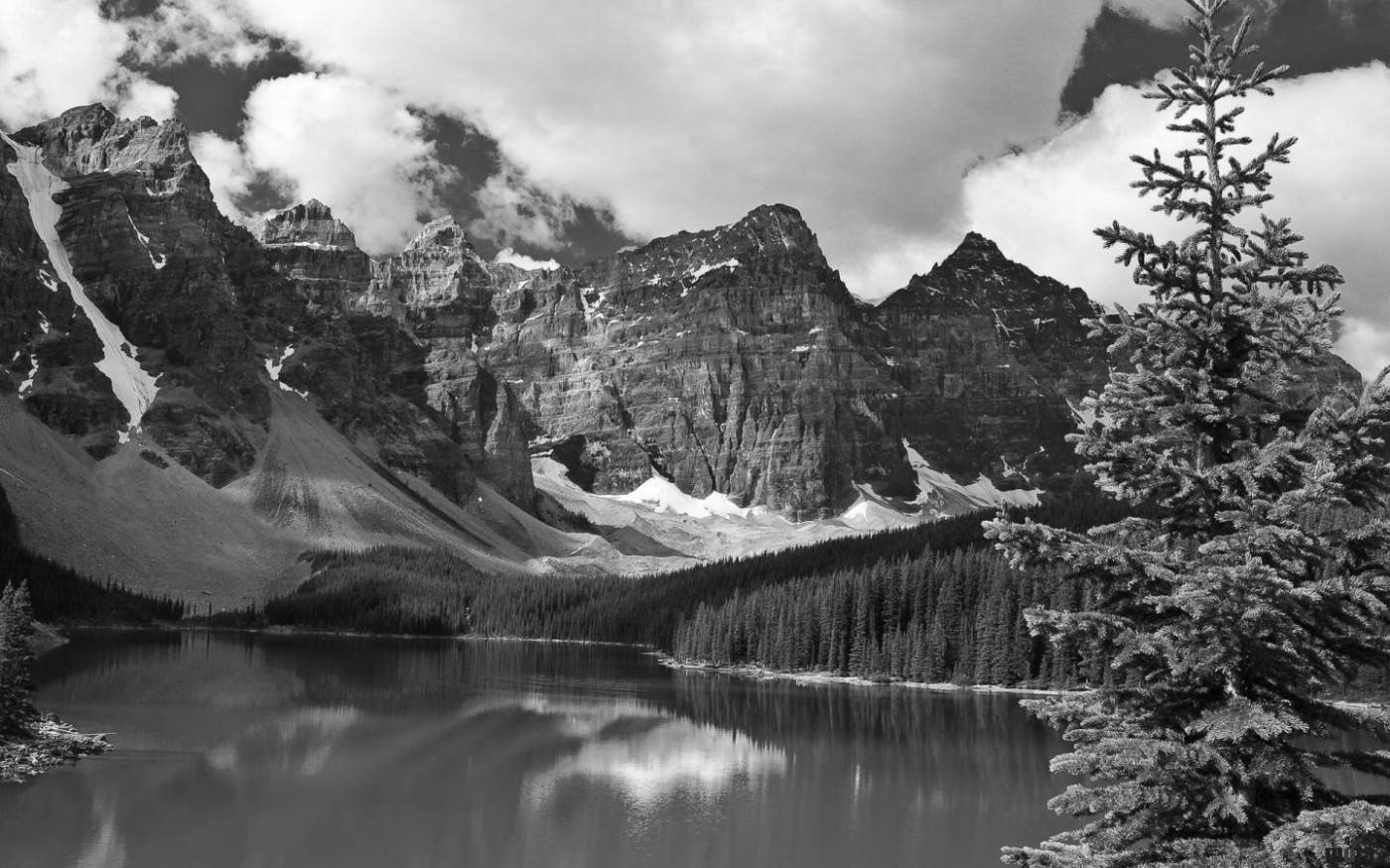 山景 桌布 壁紙 — 一個戲劇性的黑白山湖場景，白雪覆蓋的山峰倒映在平靜的水面上，四周環繞著常青樹。