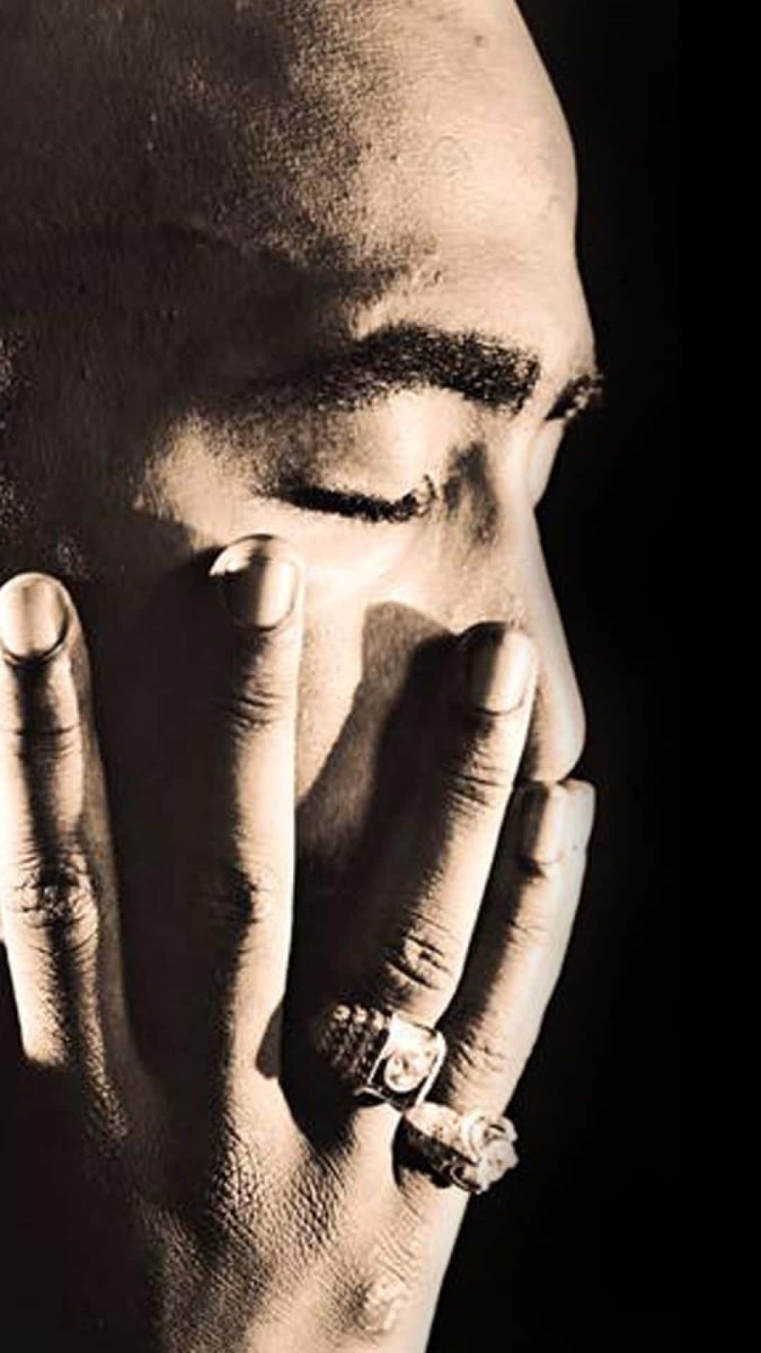 tupac 桌布 壁紙 — 一個戲劇性的黑白特寫，男人的臉被手遮住一半，在聚焦燈光下顯示細緻的皮膚質感和戒指。