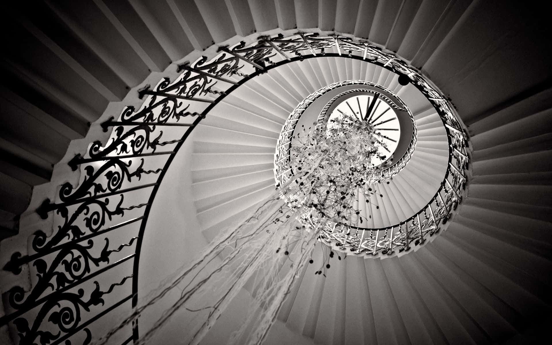 stairs 桌布 壁紙 — 一個戲劇性的黑白螺旋樓梯，帶有華麗的鐵製欄杆和從中央懸掛的水晶吊燈。