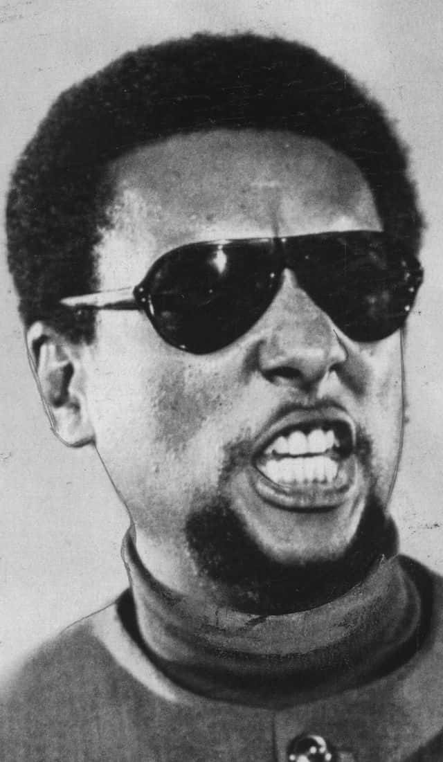 Black Panther Party 桌布 壁紙 — 一個戴太陽眼鏡的男人的黑白特寫，他露出牙齒，表情強烈。