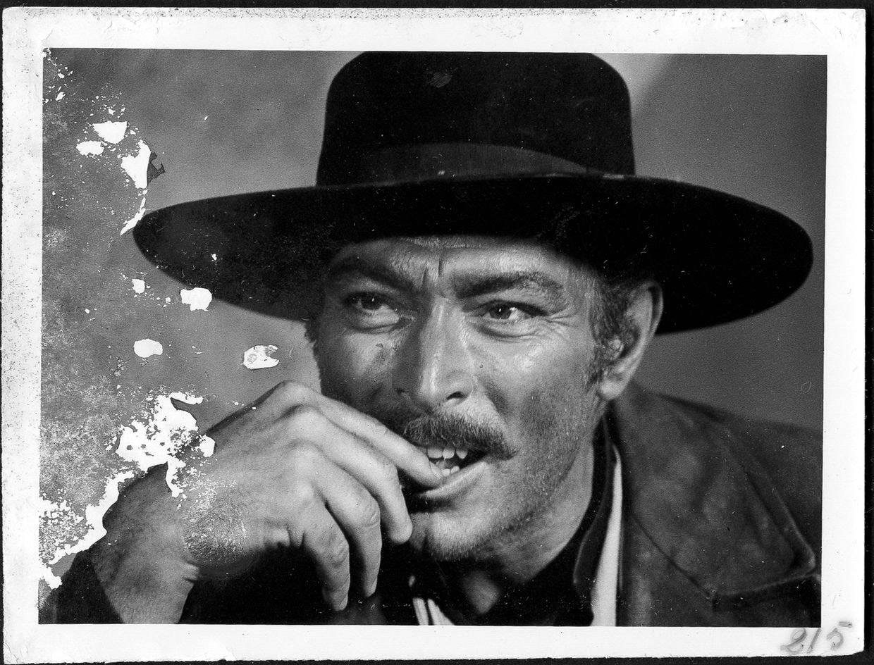 actor 桌布 壁紙 — 一個戴寬邊帽、留鬍子的男人，手靠近嘴邊，以風化背景襯托的粗糙黑白肖像。