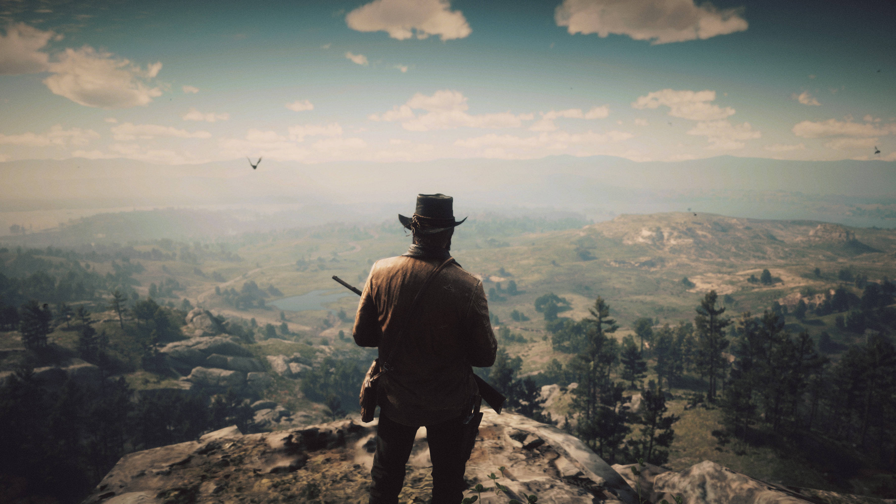 Red Dead Redemption 2 Desktop 桌布 壁紙 — 一個戴帽子的孤獨牛仔站在岩石懸崖上，俯瞰著廣闊的霧氣山谷，遠處有山脈和散落的樹木，天空部分多雲。