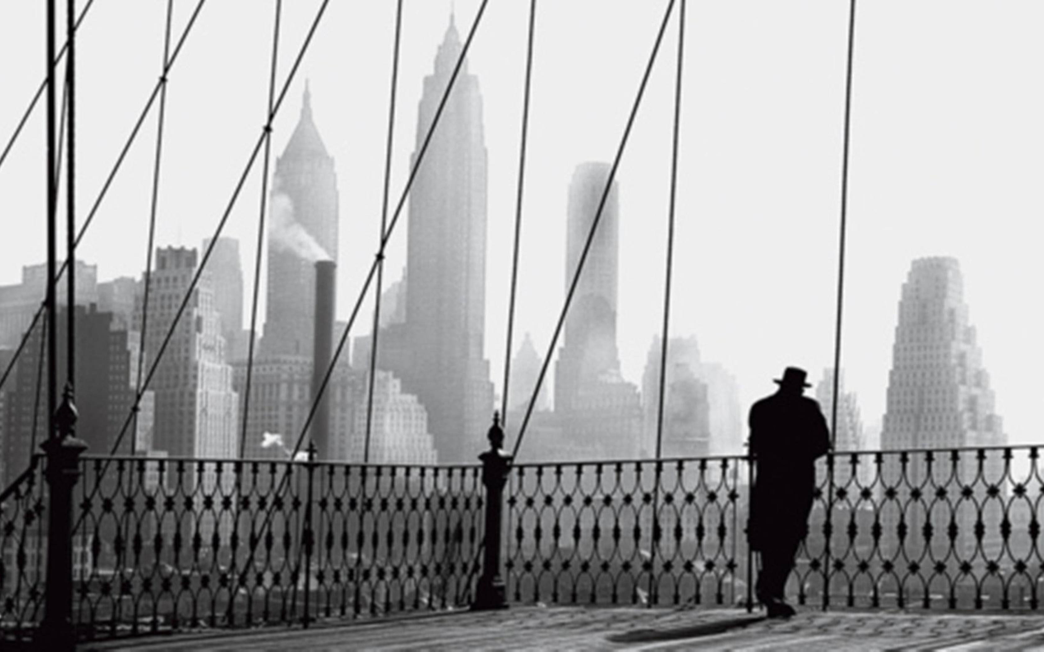 Brooklyn Bridge 桌布 壁紙 — 一個戴帽子的孤獨男子以剪影站在橋欄杆上，俯瞰著煙霧瀰漫、高樓聳立的城市天際線。