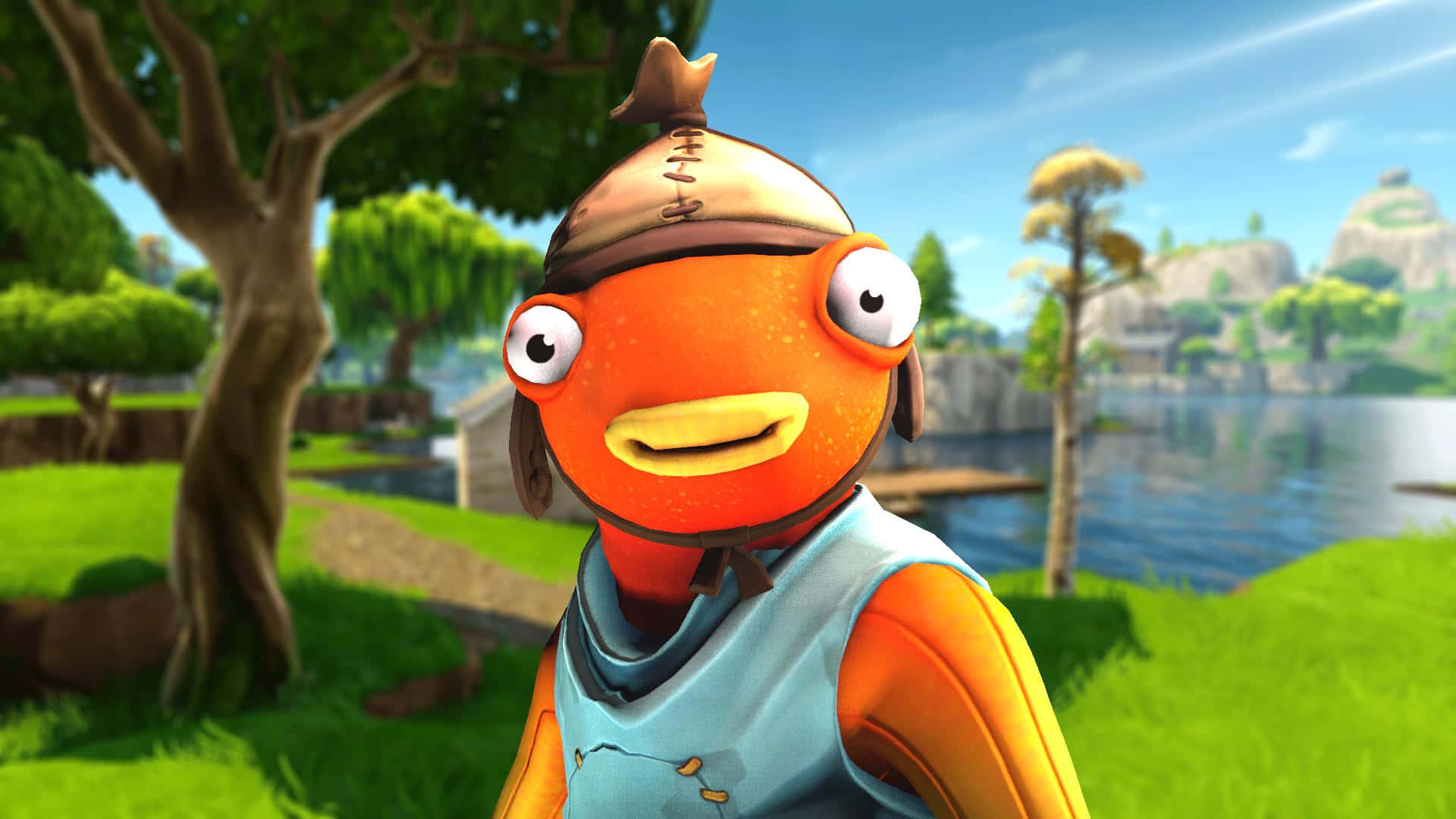 game 桌布 壁紙 — 一個戴帽子的橙色開心魚角色，在平靜的湖邊一片明亮的綠色草地上微笑。