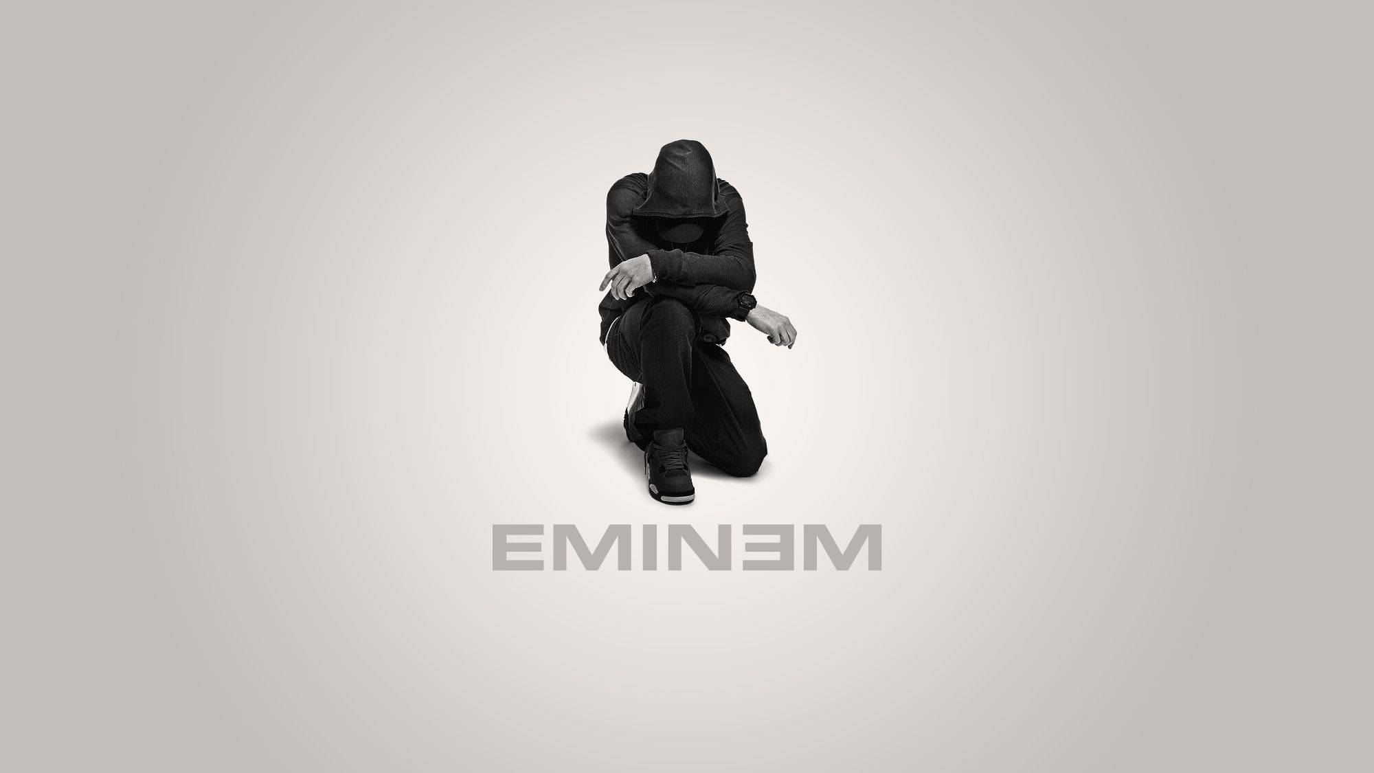 Eminem 桌布 壁紙 — 一個戴帽子的身影蹲在陰影中，背景為純灰色，下方有名字「EMINEM」。