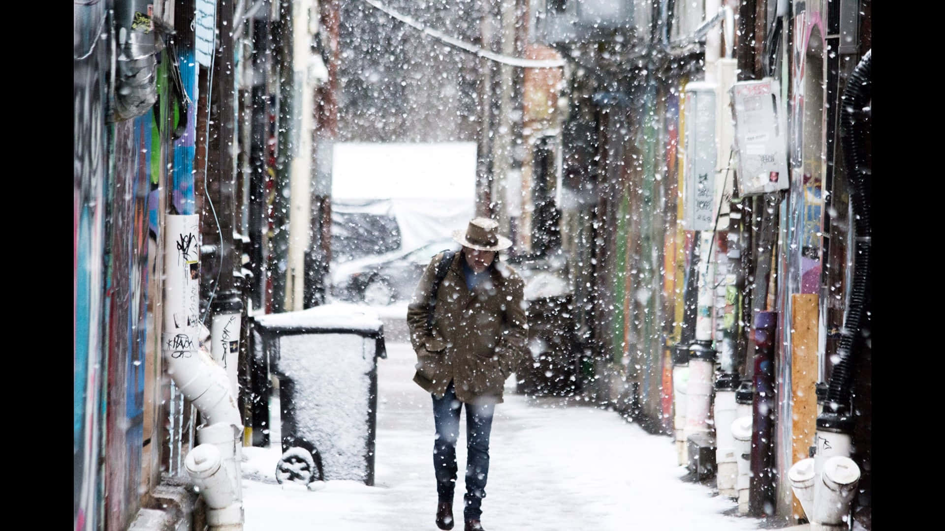Woman 桌布 壁紙 — 一個戴帽穿外套的人走過一條狹窄的雪巷，兩旁是佈滿塗鴉的牆壁和積雪覆蓋的管道。