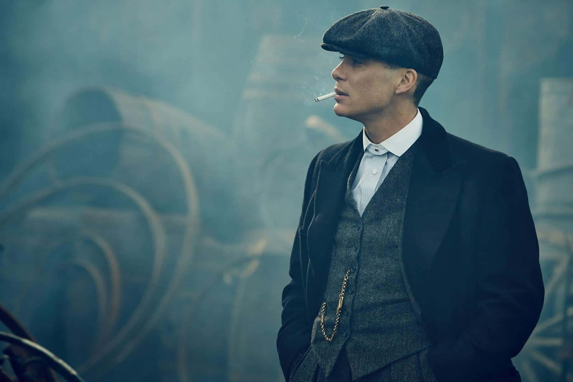 身穿復古西裝和帽子的男人在煙霧繚繞的工業環境中抽煙。 — Peaky Blinders 壁紙