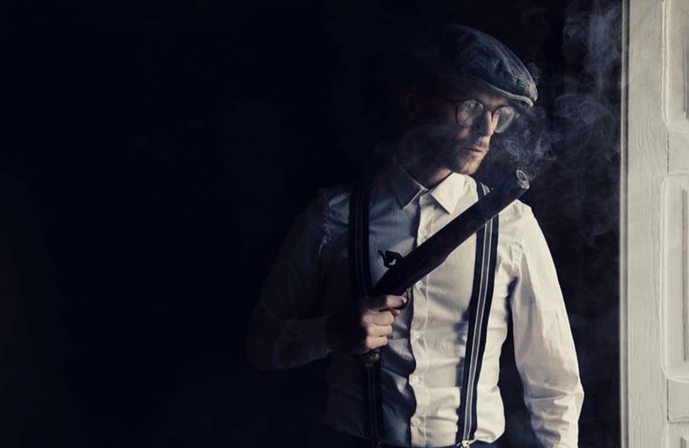 Mafia 桌布 壁紙 — 一個戴平頂帽和吊帶的男人在昏暗的房間裡拿著冒煙的煙斗，煙霧在他周圍盤旋。