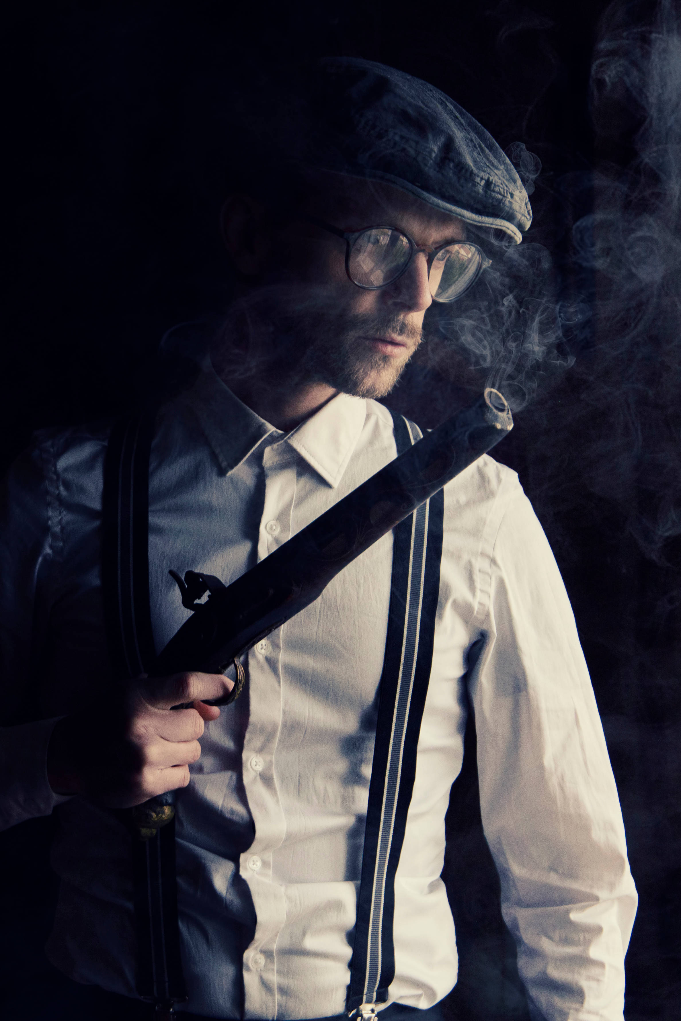 Hitman Black 桌布 壁紙 — 一個戴平頂帽和眼鏡的男人在黑暗背景下抽煙斗，煙霧繚繞。