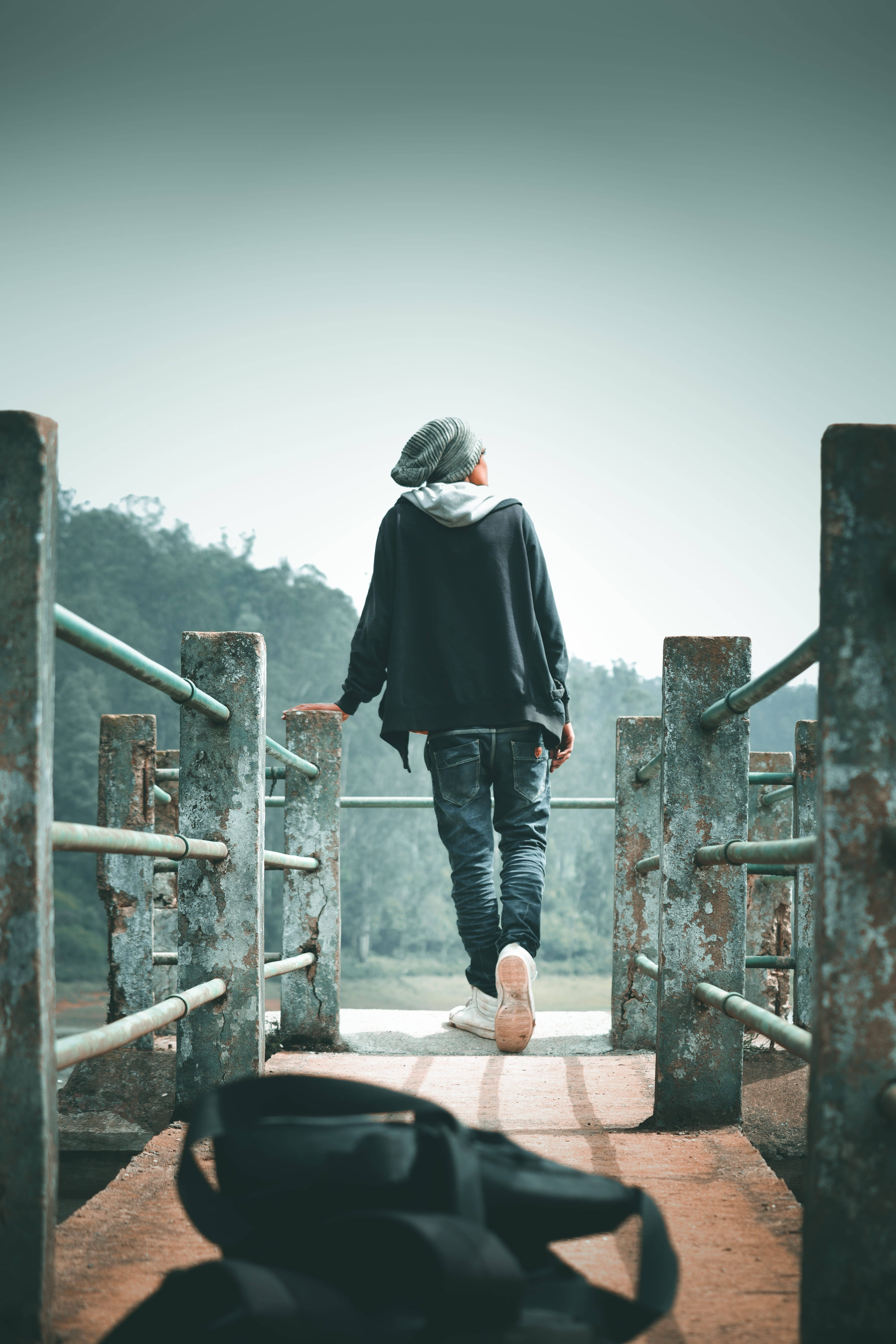 walking away 桌布 壁紙 — 一個戴毛帽和連帽衫的人背著背包在風化的橋上走遠。