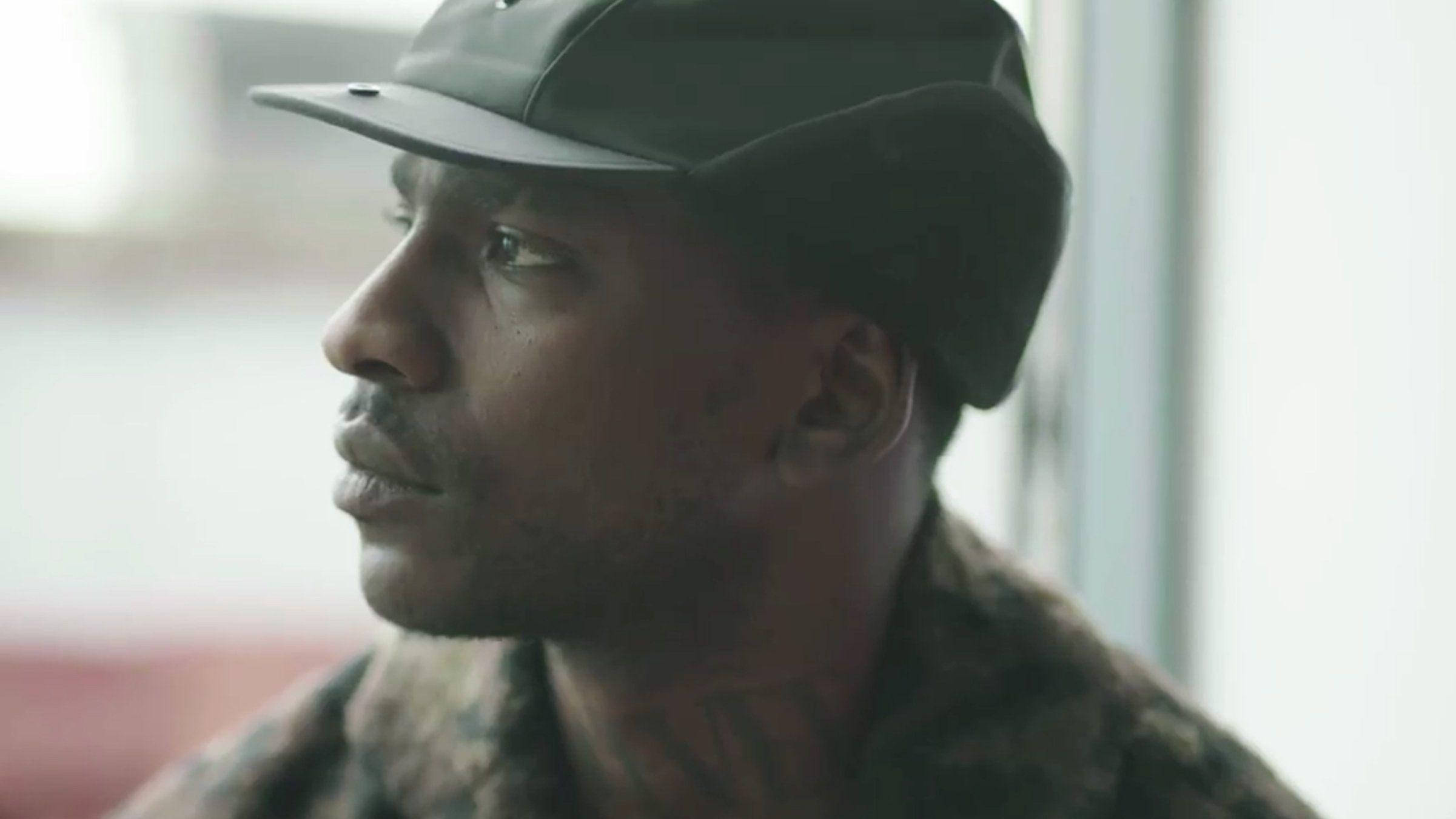 Skepta 桌布 壁紙 — 一個戴深色帽子的男人若有所思地望向窗外，柔和自然光凸顯他的側面和頸部刺青。