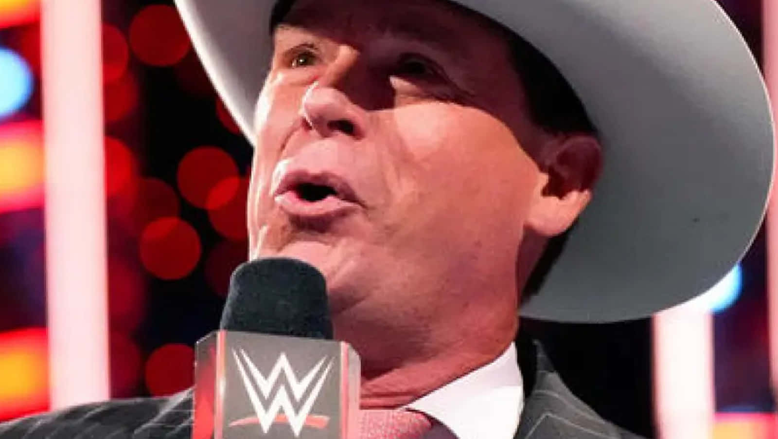 WWE 桌布 壁紙 — 一個戴白色牛仔帽的男人對著WWE麥克風說話，背景是色彩繽紛的散景。