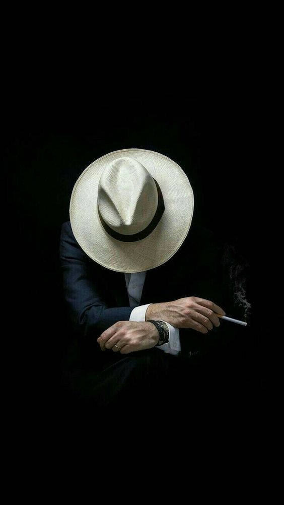 bad 桌布 壁紙 — 一個戴白色紳士帽、穿西裝的神秘人物，在純黑背景前拿著香煙。