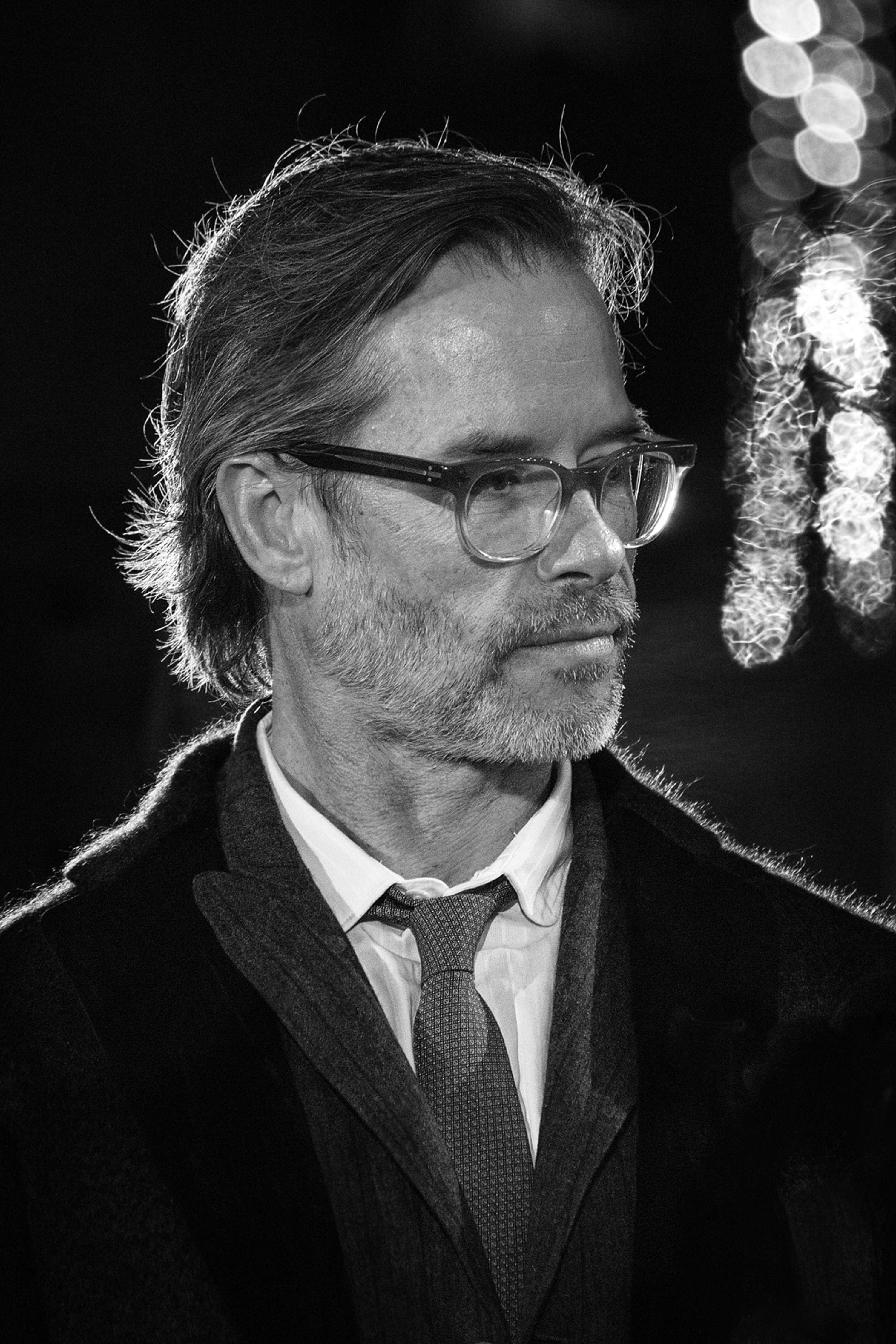 Guy Pearce 桌布 壁紙 — 一個戴眼鏡、留鬍子的男人的黑白肖像，在散景照明背景下若有所思地望向一邊。