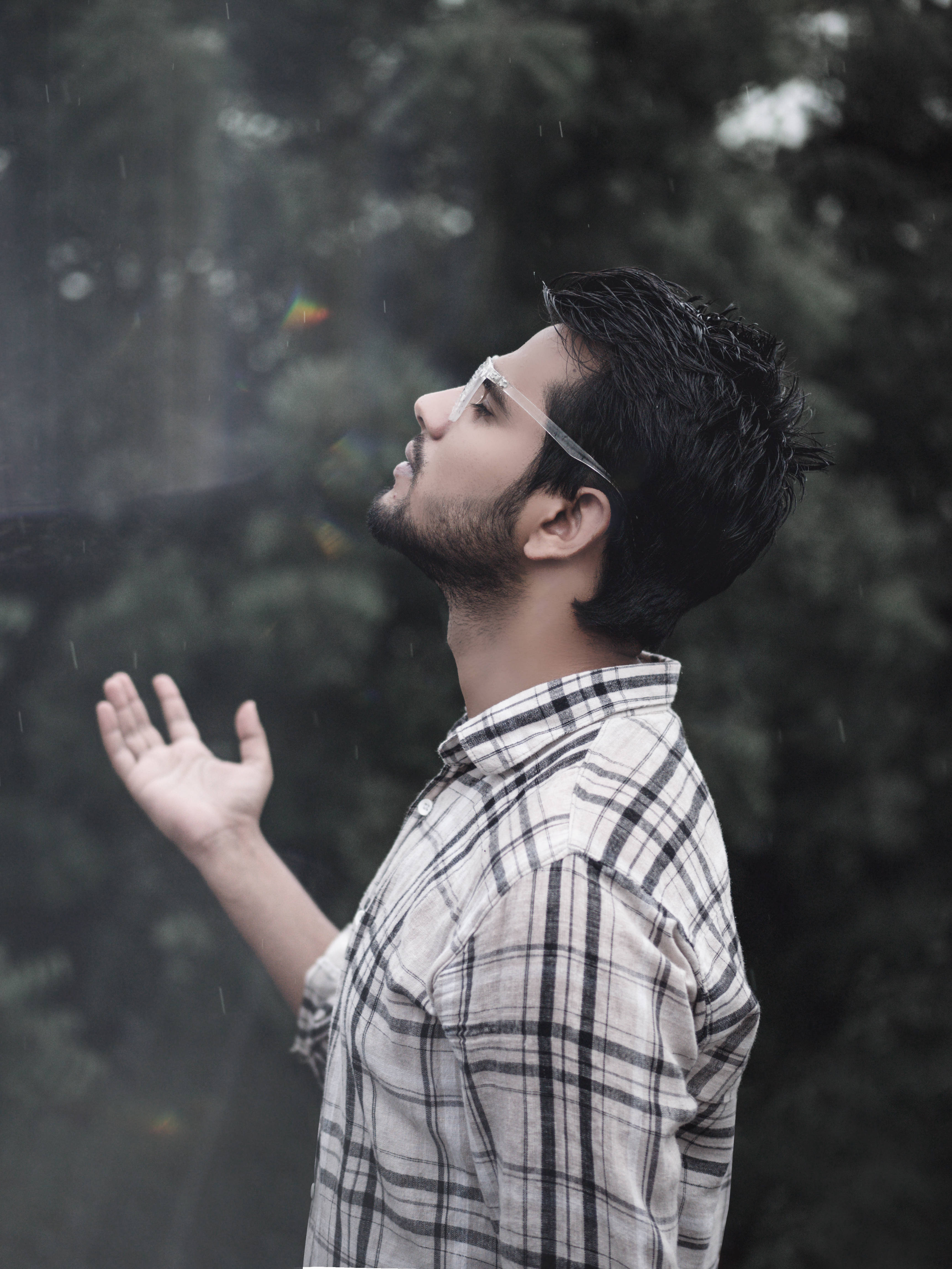 Feels 桌布 壁紙 — 一個戴眼鏡、穿著格紋襯衫的男人站在雨中，舉起手，周圍有雨滴落下。