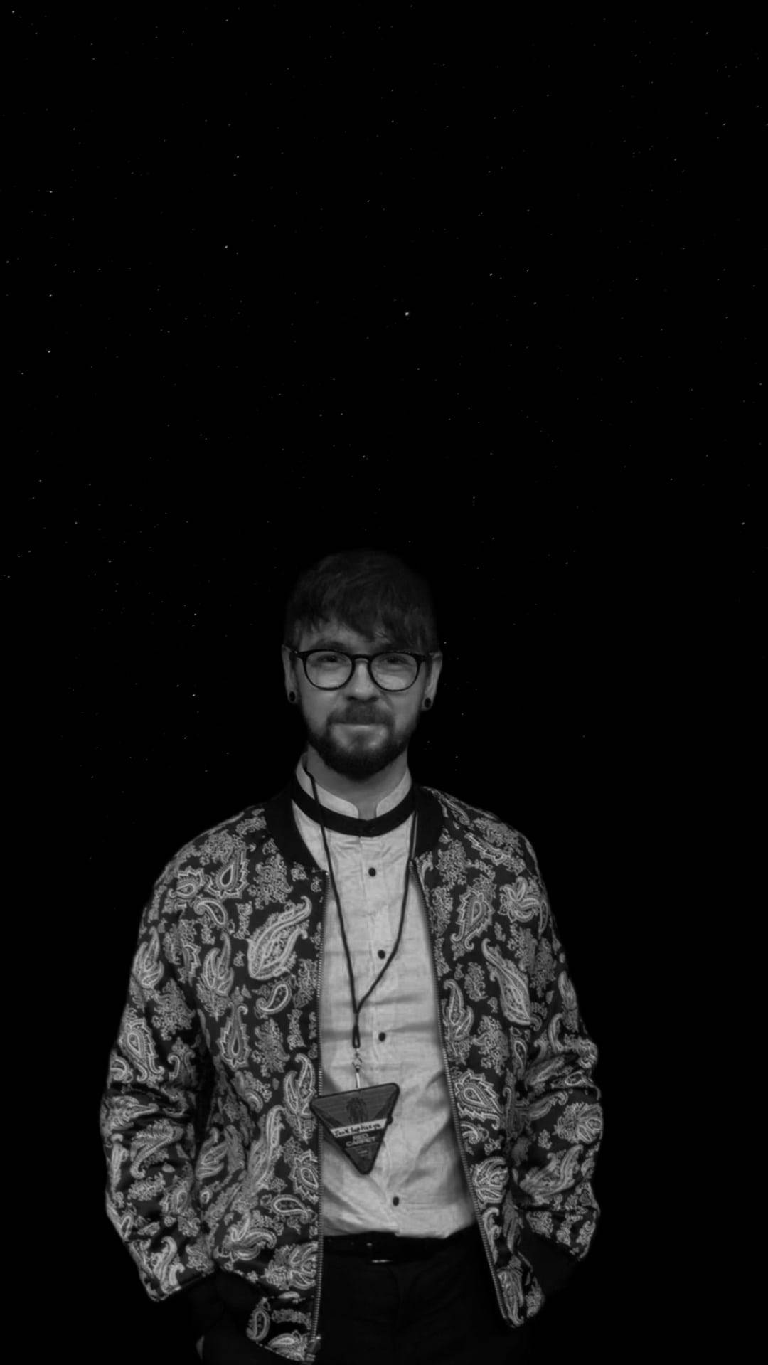Jacksepticeye 桌布 壁紙 — 一個戴眼鏡、身穿圖案外套的男人，站在單色的星空夜空下。