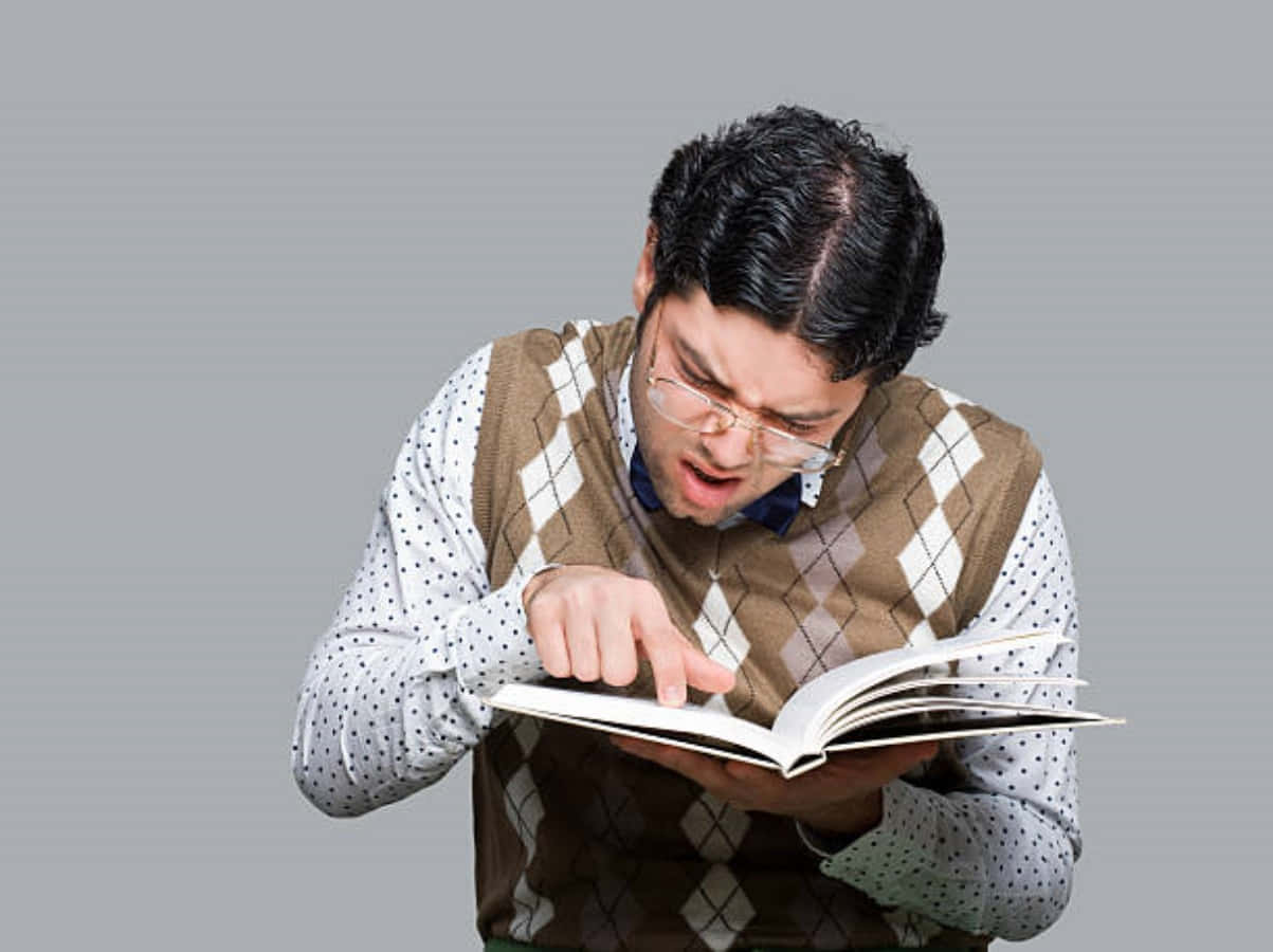 Nerd 桌布 壁紙 — 一個戴眼鏡、身穿棕色菱形花紋背心的男人，指著一本書，表情震驚。
