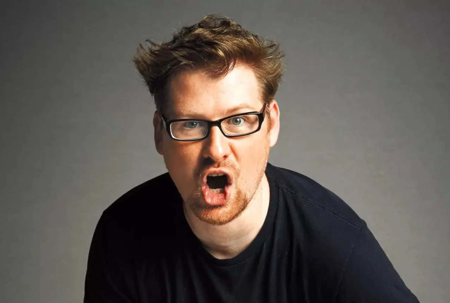 Justin Roiland 桌布 壁紙 — 一個戴眼鏡、頭髮凌亂的男人對著純灰色背景直接向鏡頭尖叫。
