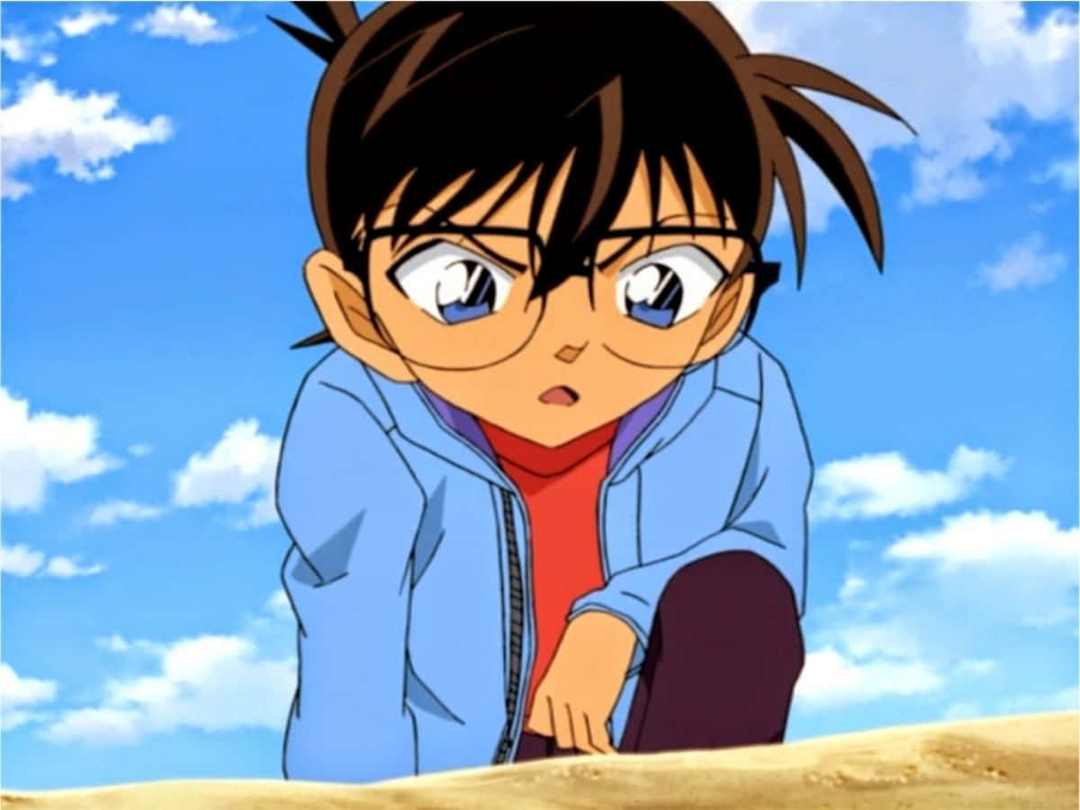 Detective Conan 桌布 壁紙 — 一個戴眼鏡、頭髮豎起的年輕動漫男孩，在晴朗藍天和 fluffy 白雲下的沙地上蹲著。