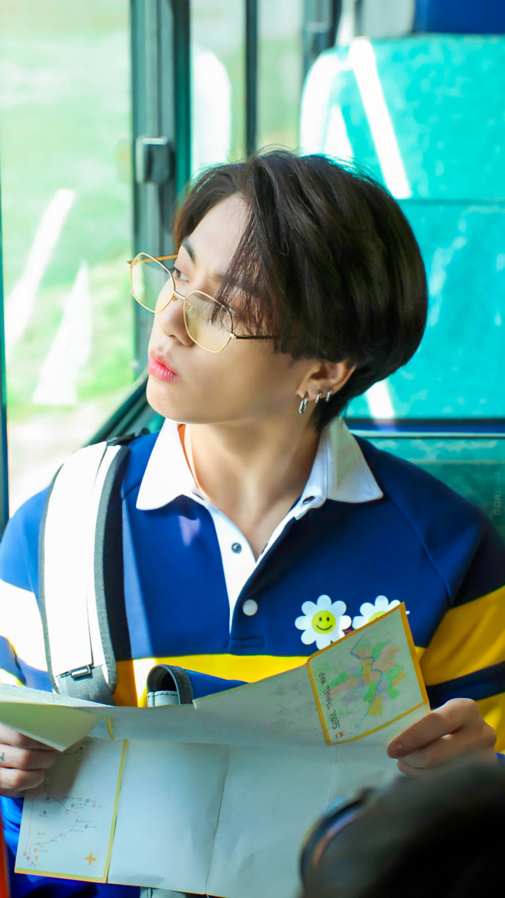 Jungkook 桌布 壁紙 — 一個戴眼鏡和背包的年輕人，拿著色彩繽紛的地圖，望向巴士窗外。