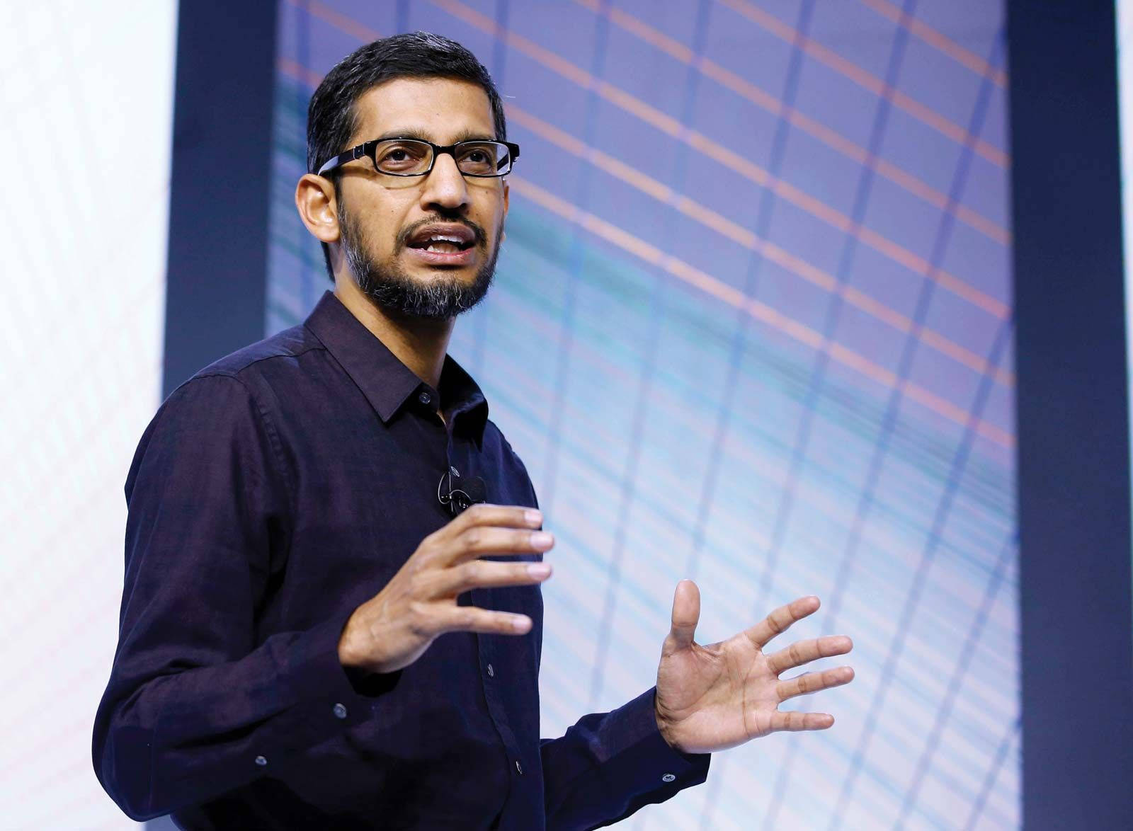 google 桌布 壁紙 — 一個戴眼鏡和鬍鬚的男人在色彩繽紛的幾何背景前在舞台上熱情地演講。