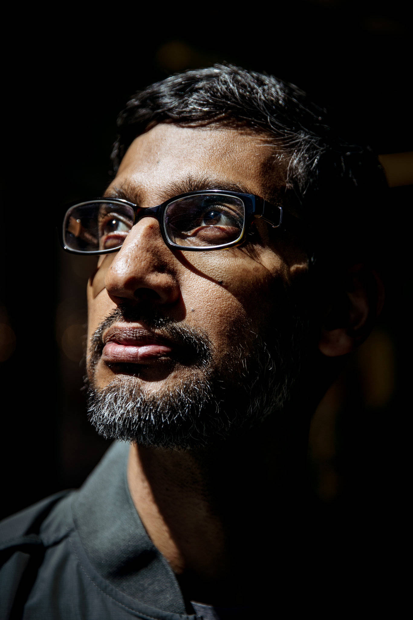 google 桌布 壁紙 — 一個戴眼鏡和鬍鬚的男人在黑暗背景下，以戲劇性的明暗對比肖像向上凝視。
